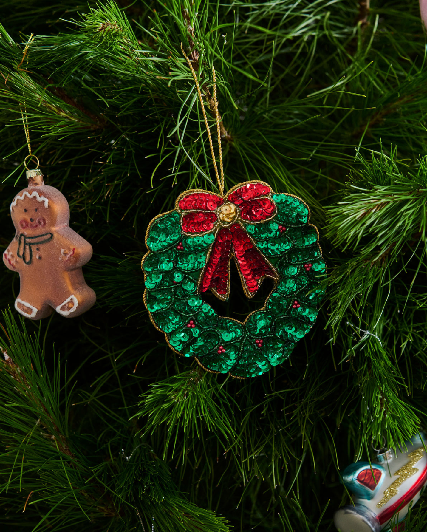 Decorative Christmas wreath ornament with a red bow hanging on a tree.