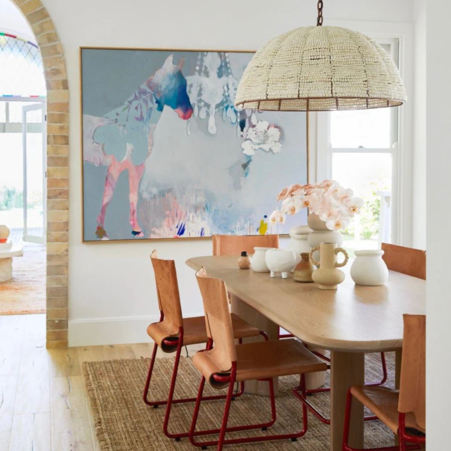 Dining room with a wooden table and chairs, abstract painting on the wall, and clay bead pendant light.