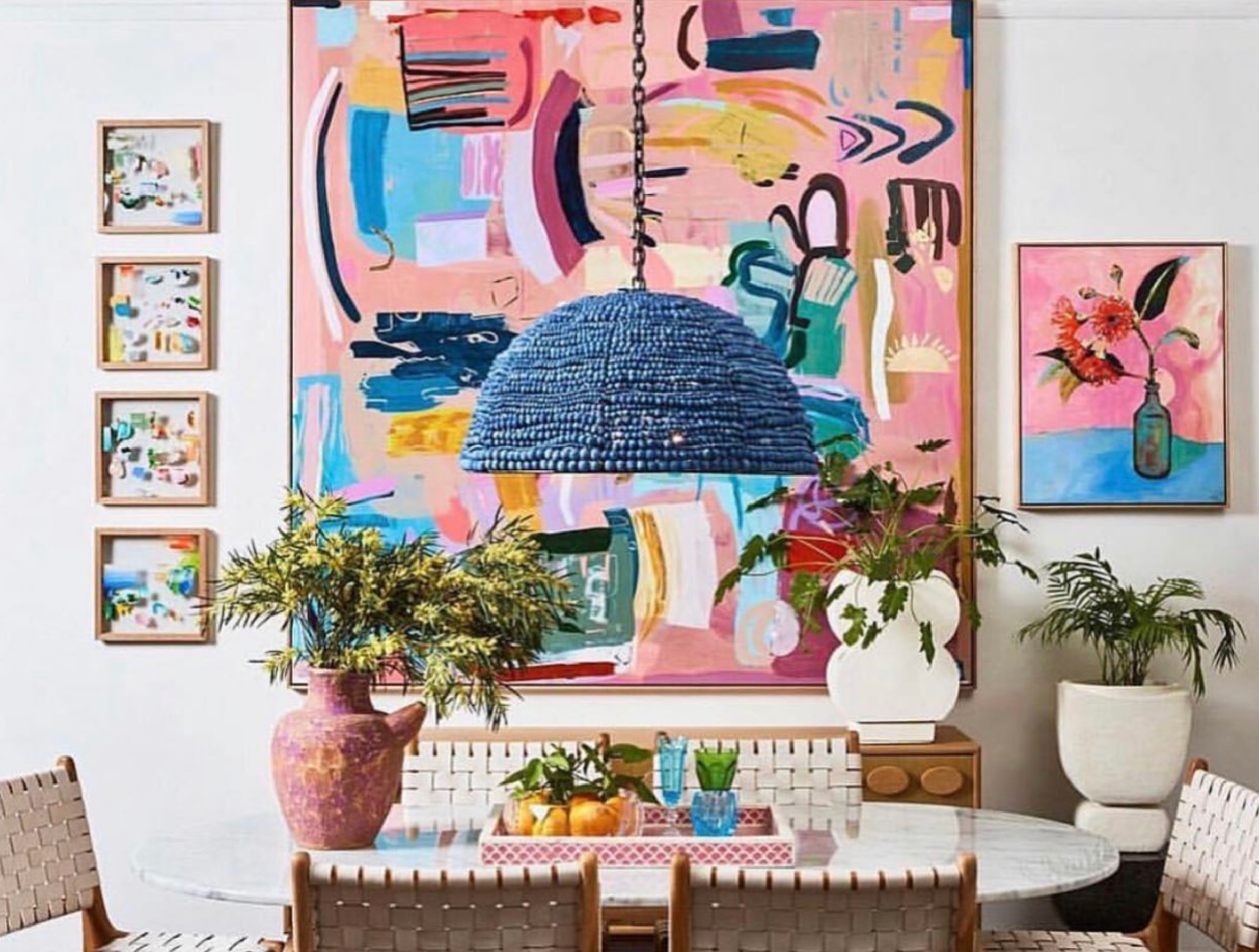 Dining room with colorful abstract art, plants, and a blue beaded pendant light.