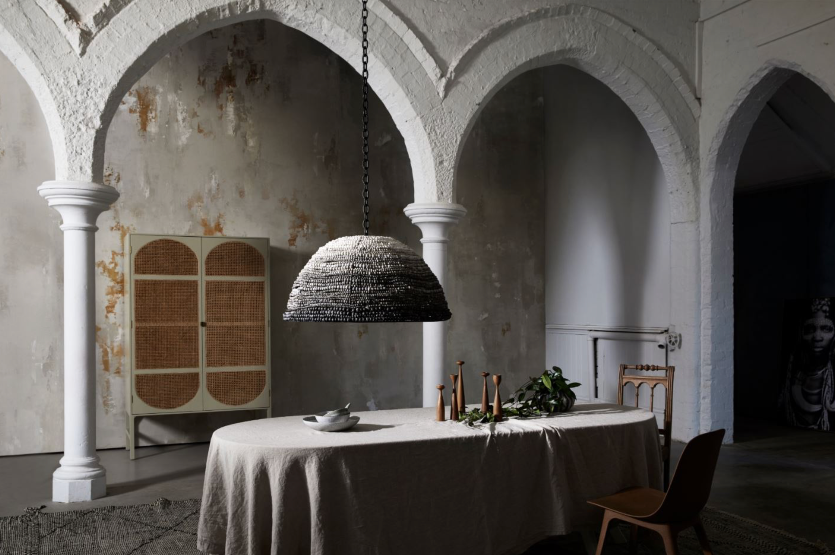 Dining table with a textured clay pendant light in an archway room