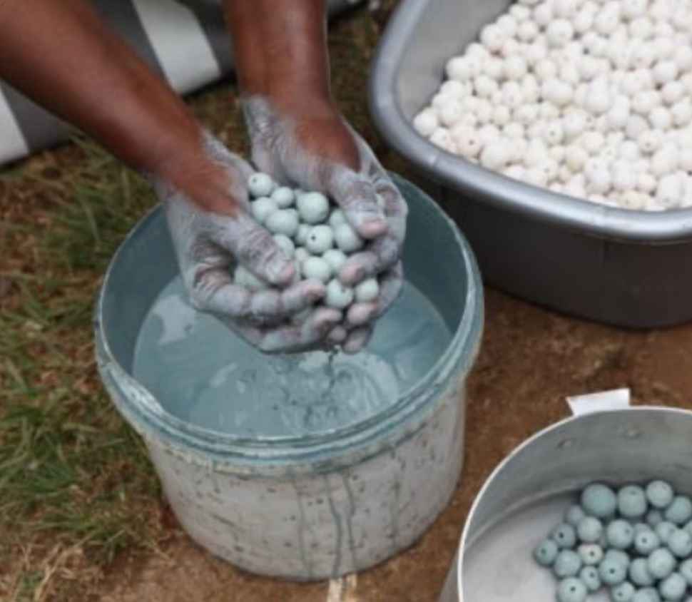 Person sorting small handmade beaded objects into a bucket of liquid