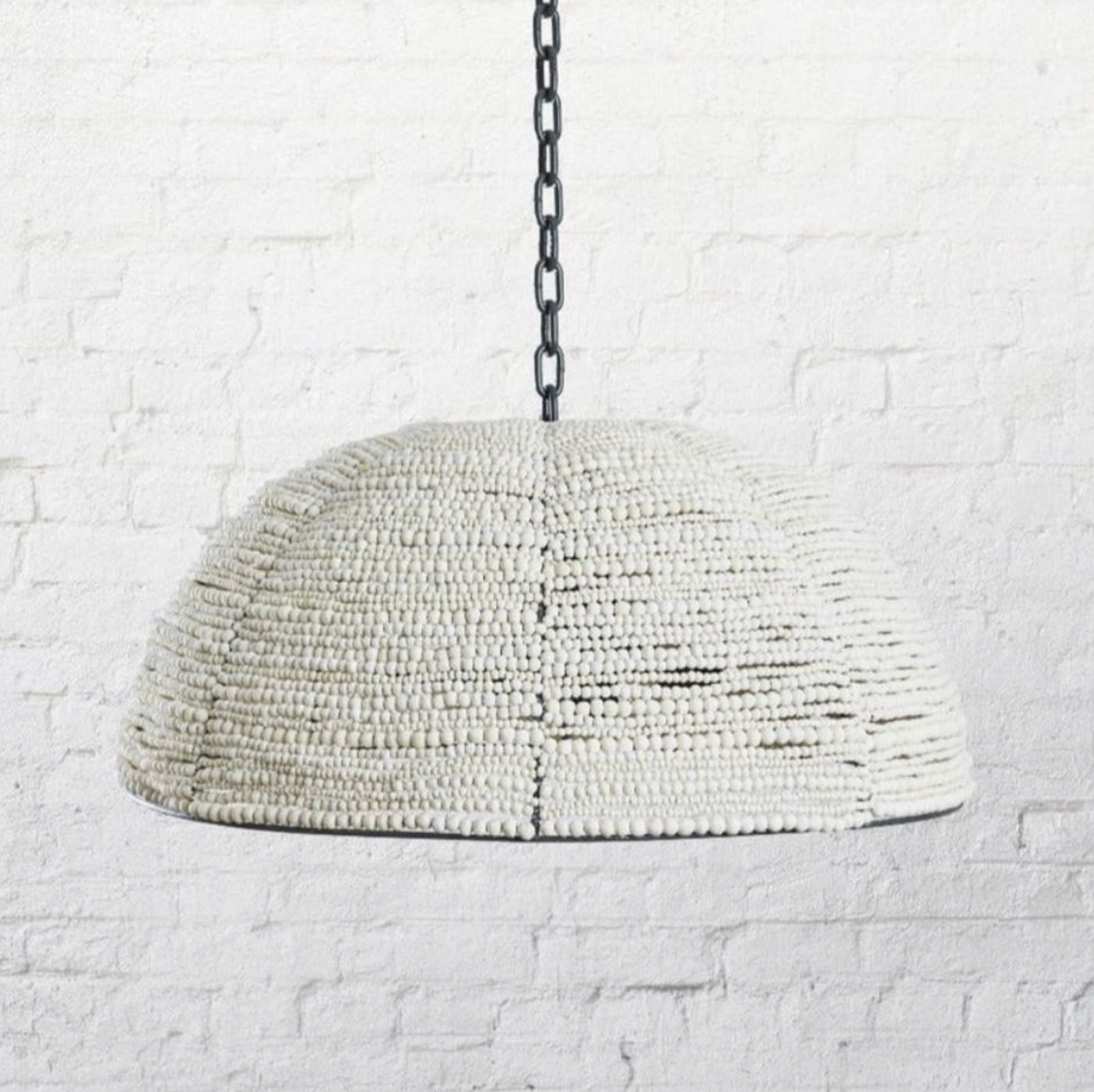 Textured clay beaded interior pendant light hanging against a white brick wall