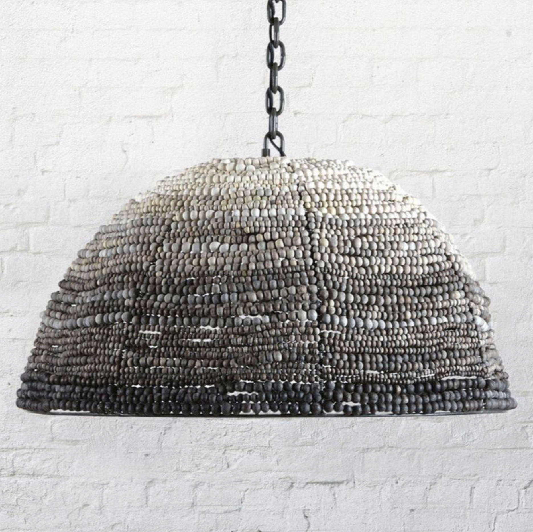 Decorative pendant light with clay beaded design hanging against a white brick wall.