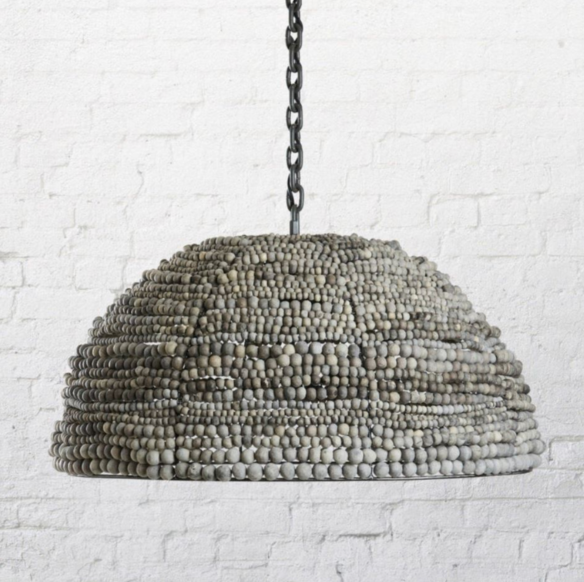 Clay beaded pendant light fixture against a white brick wall
