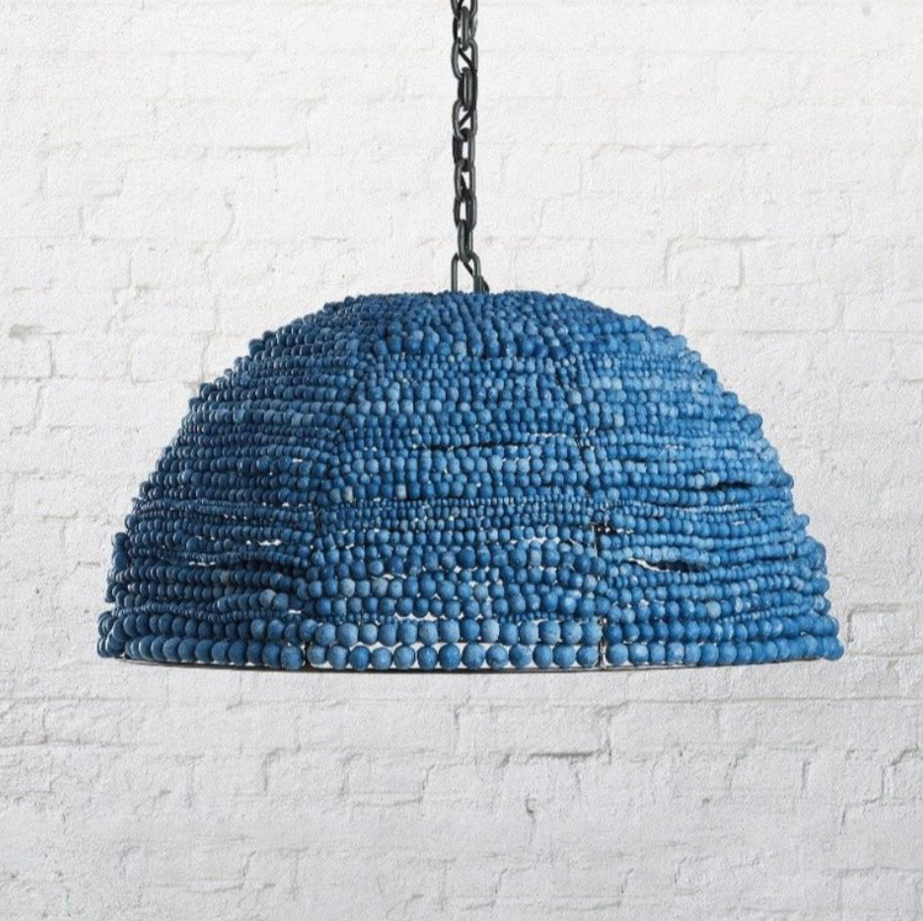 Blue beaded pendant light against a white brick wall