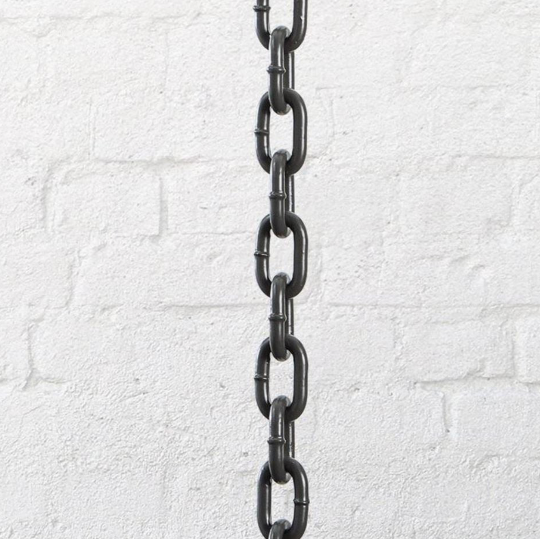 Dark coloured pendant chain hanging against a white brick wall