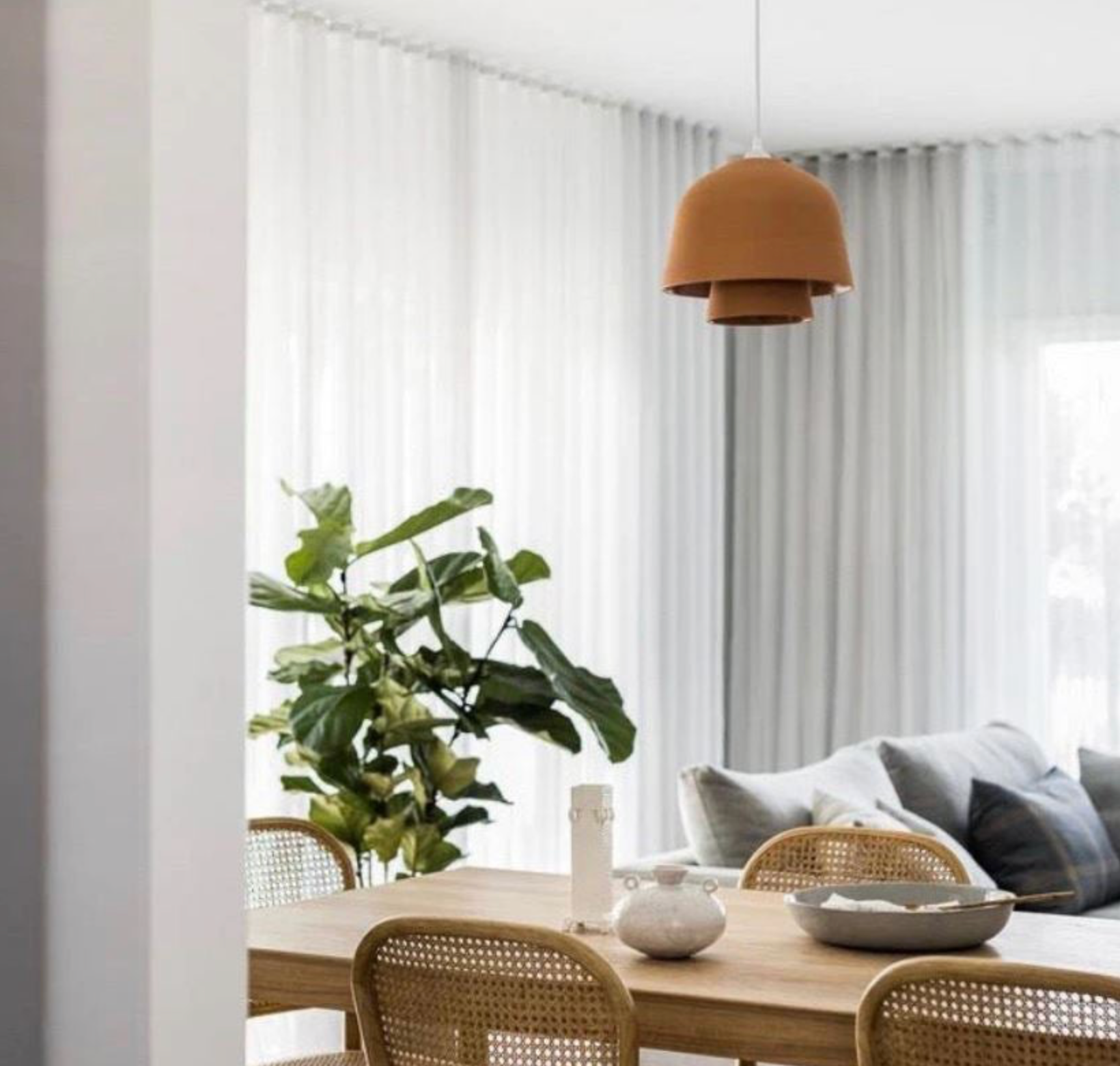 Modern dining area with wooden table, Terracotta clay pendant light, wicker chairs, and a plant.