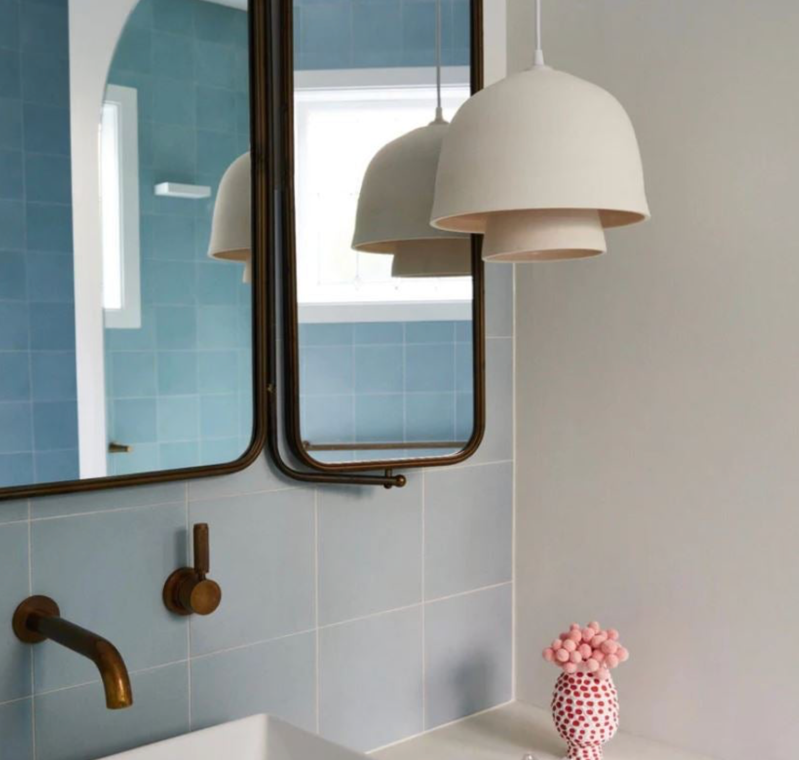 Bathroom interior with mirrors, pendant light, and a pink vase.