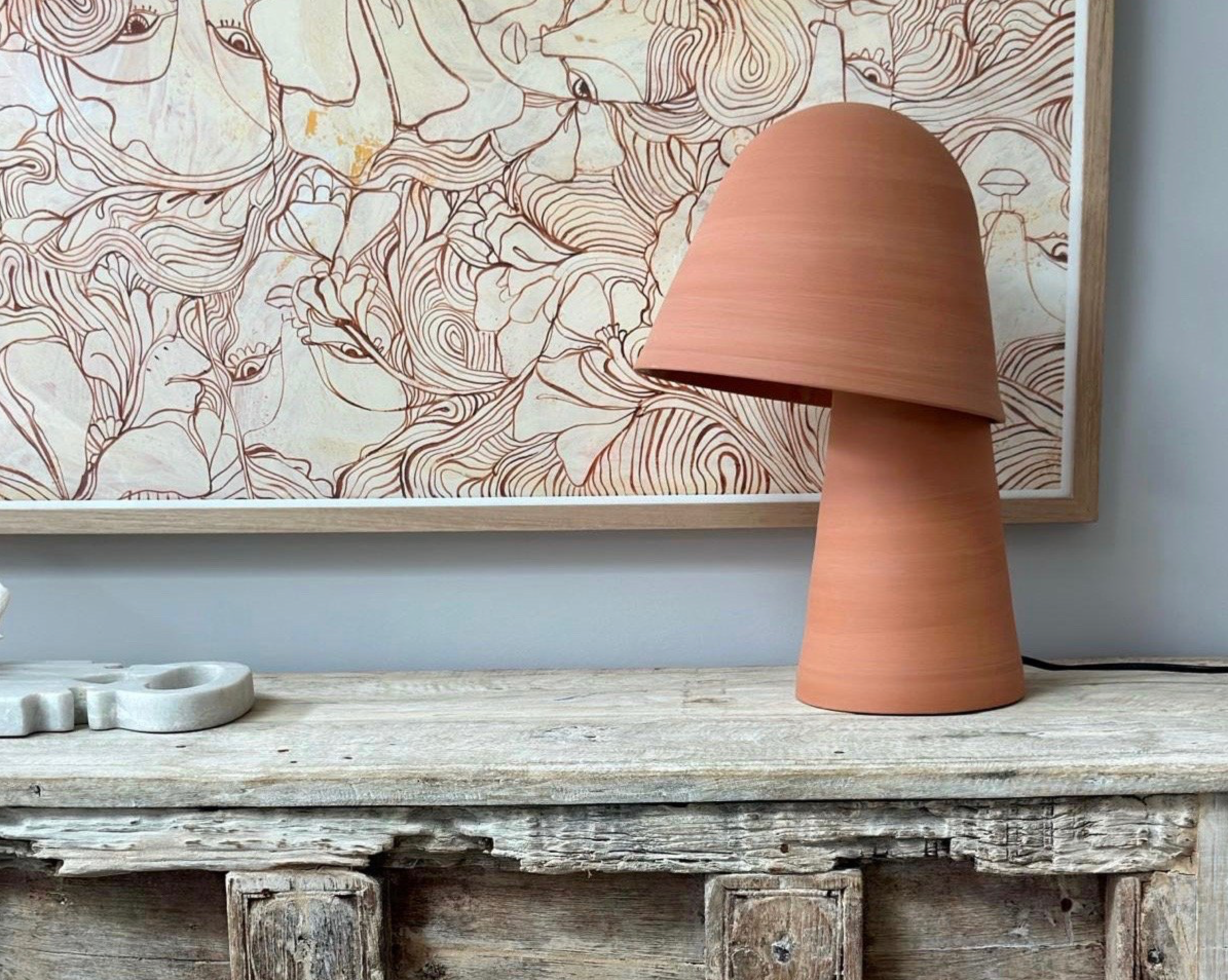 Terracotta lamp on a wooden surface with abstract art in the background