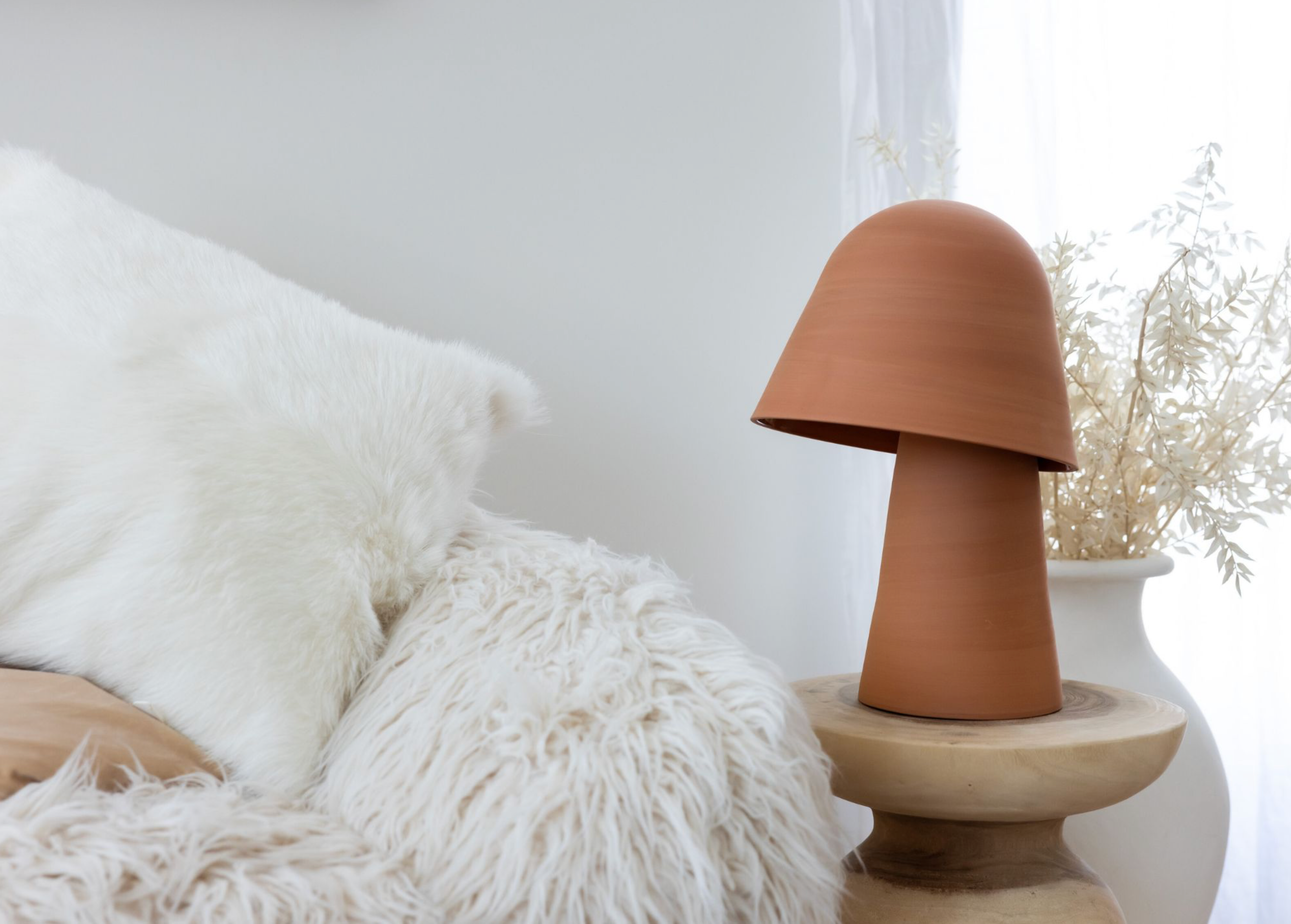 Terracotta lamp on a wooden surface with white pillows and a soft blanket in the background
