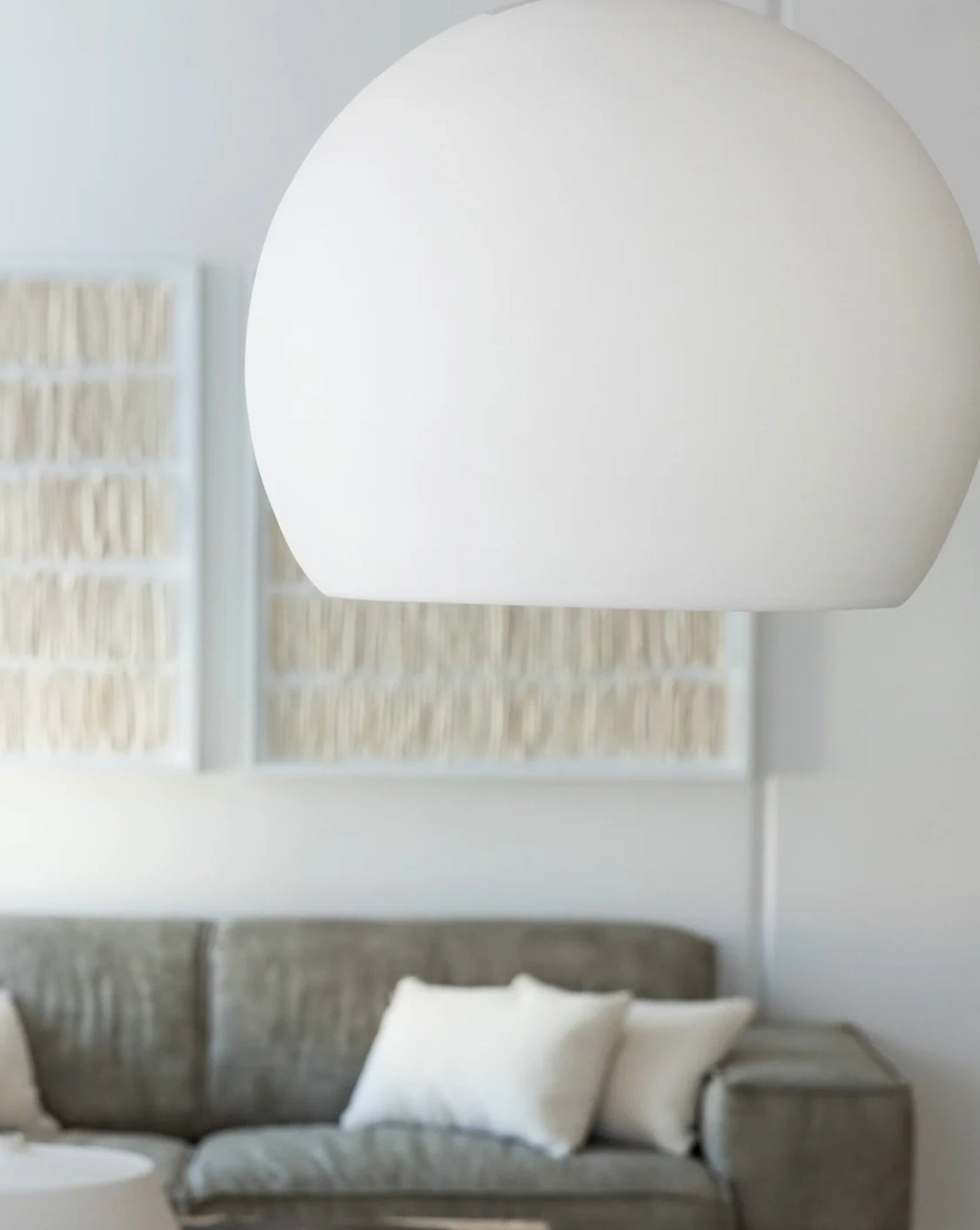 White pendant light hanging above a gray sofa in a living room.