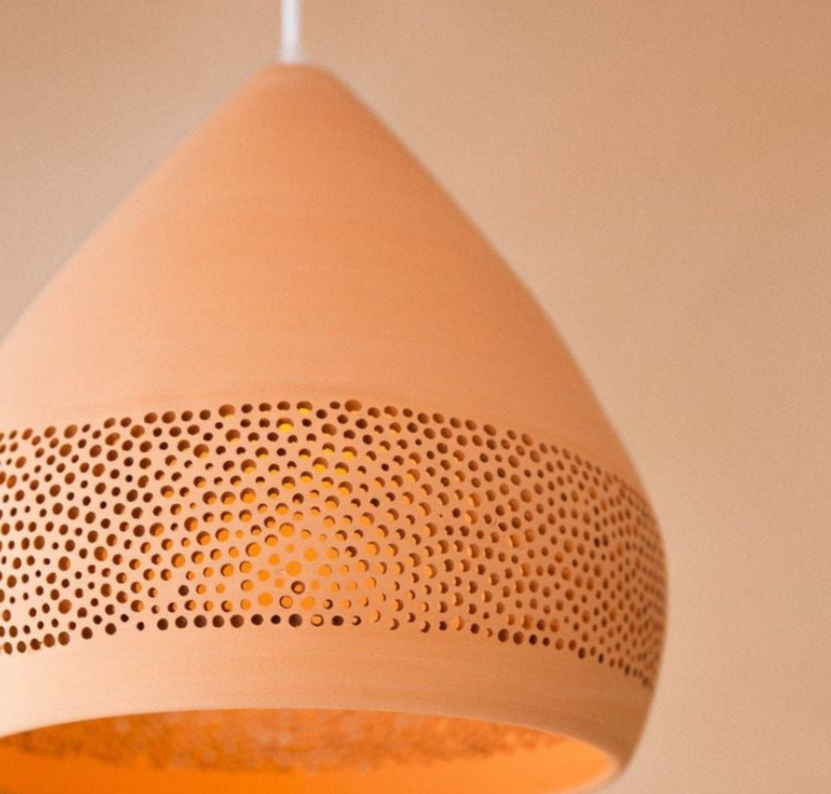 Terracotta pendant light with perforated design on a beige background
