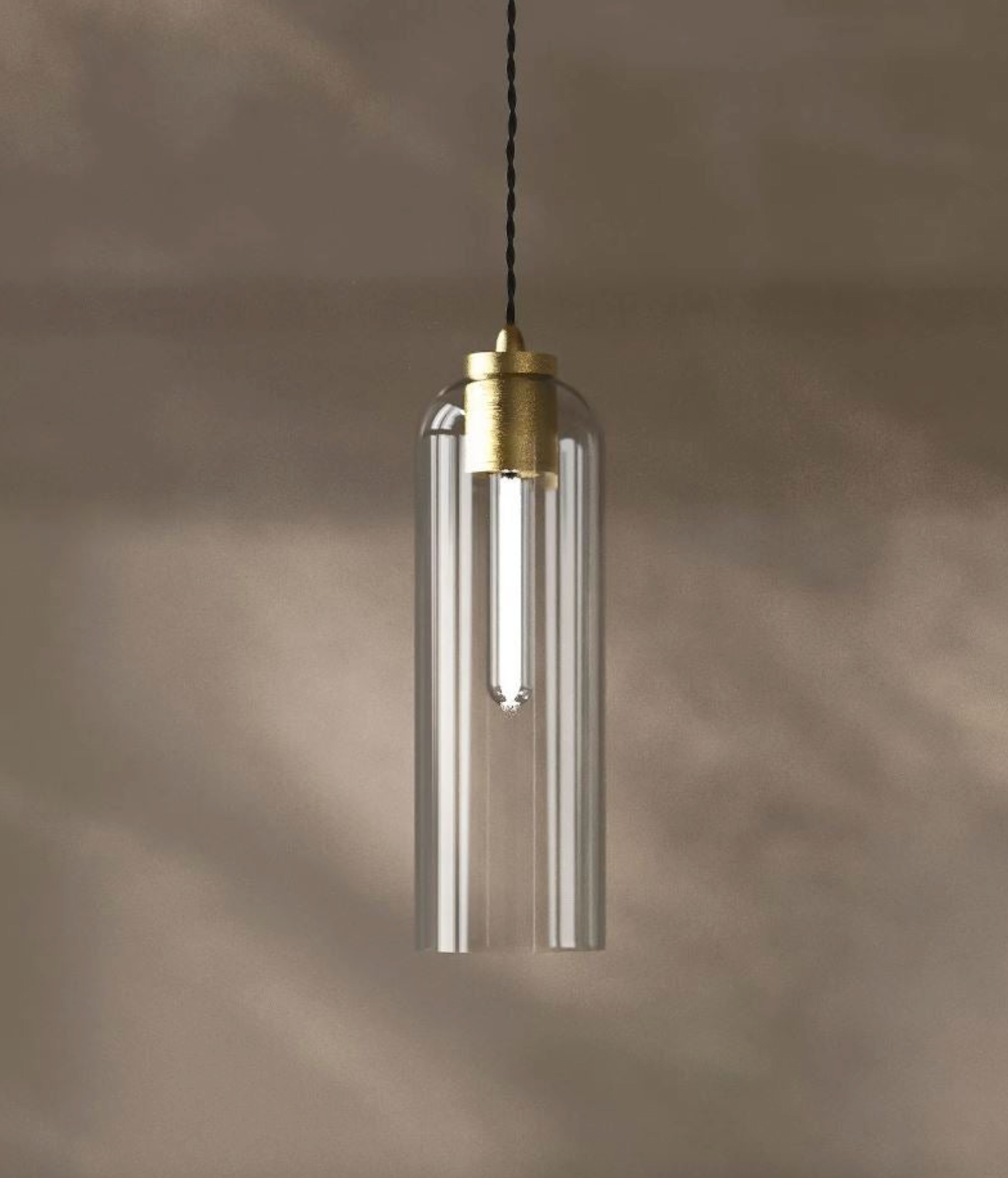 Pendant light with clear cylindrical shade and brass fitting on a neutral background
