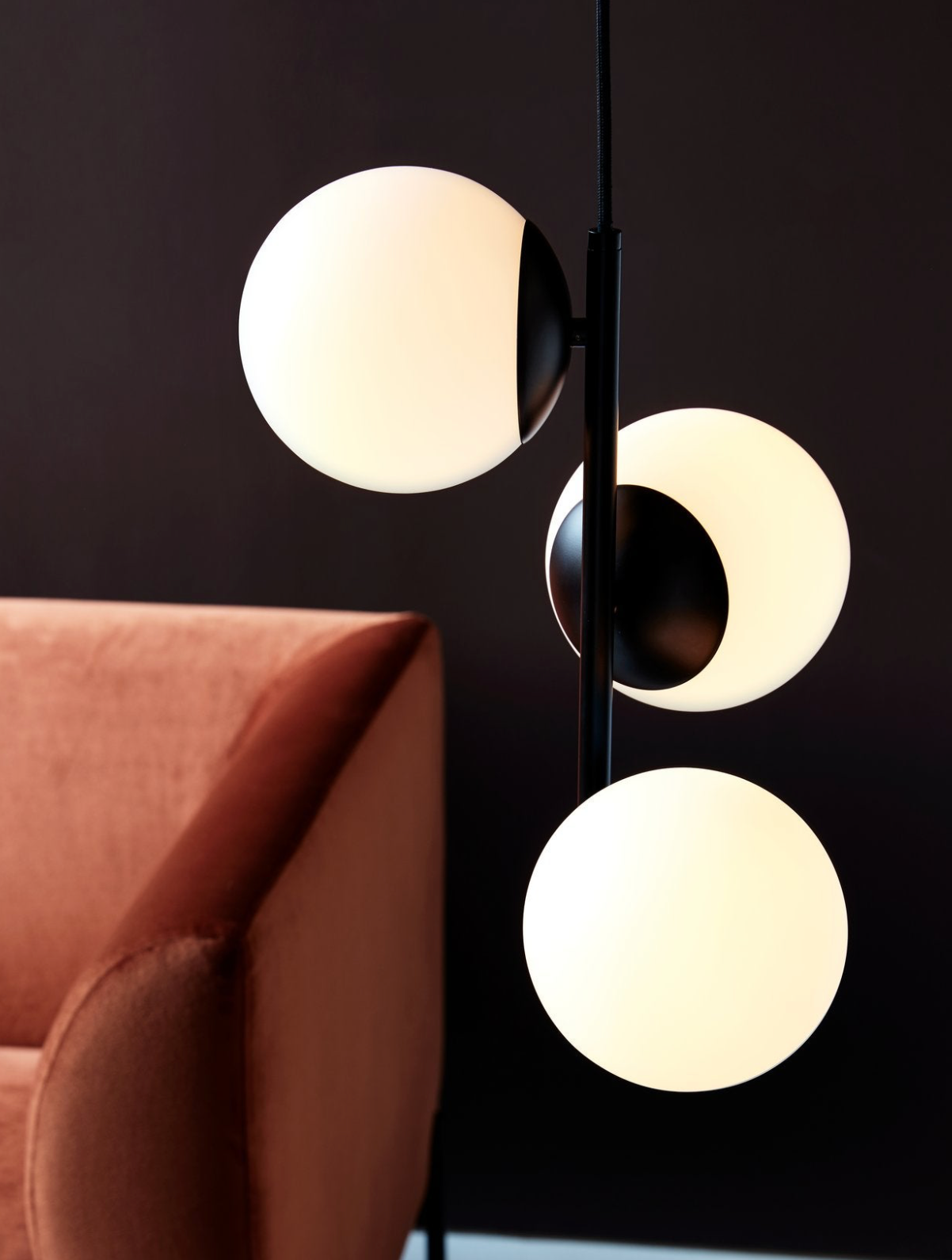 Modern pendant light fixture with three round lights against a black background