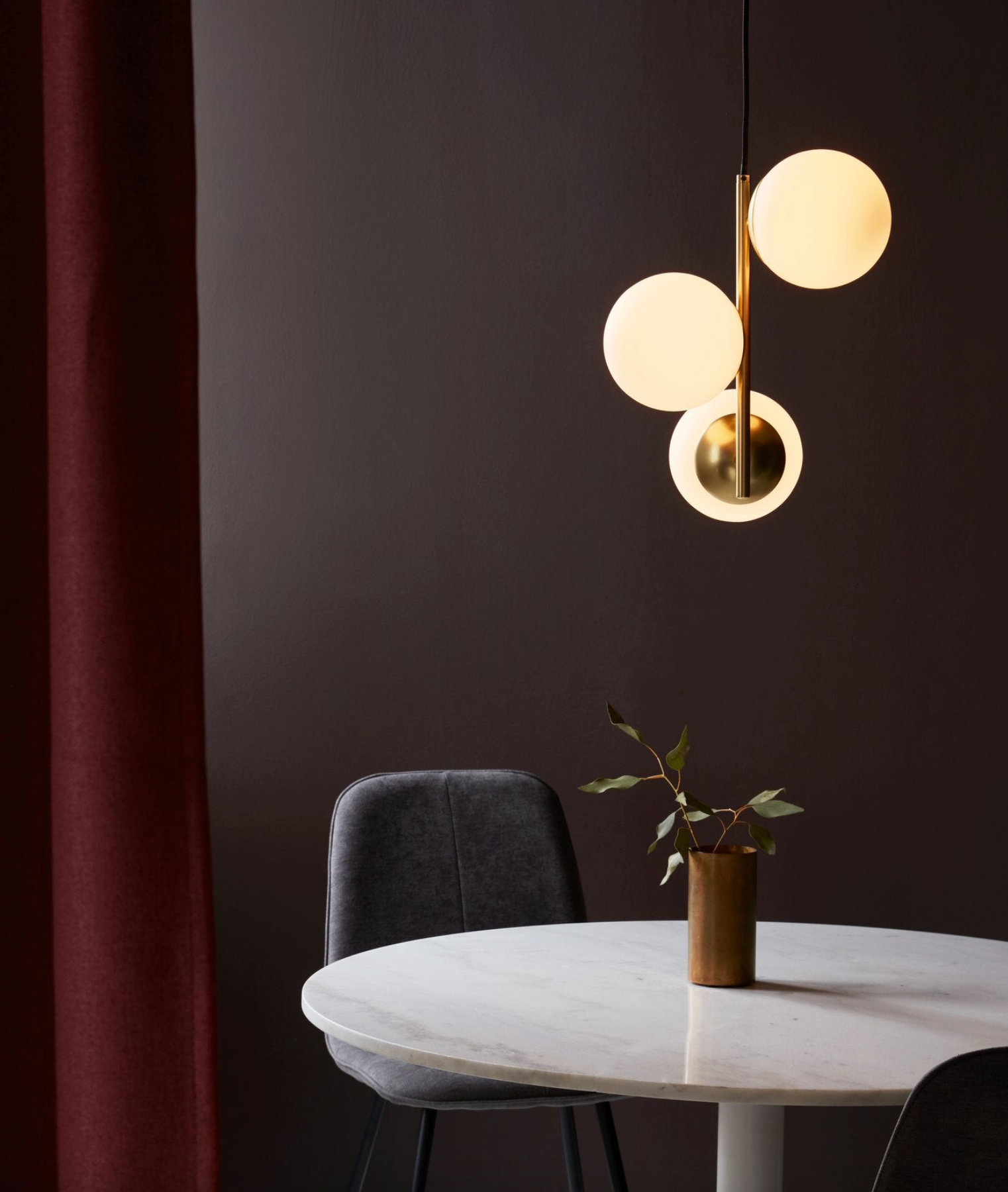 Modern pendant light fixture over a round table with a plant against a dark wall.