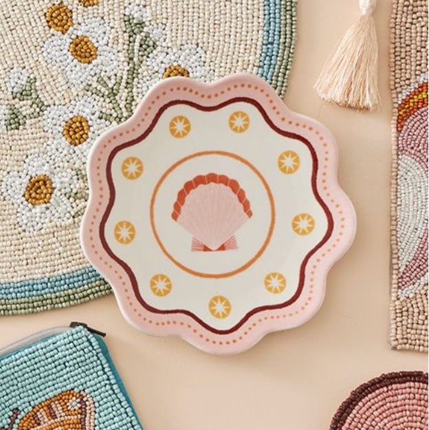 Decorative items including a beaded placemat, a decorative plate with floral design, and a tassel on a beige surface.