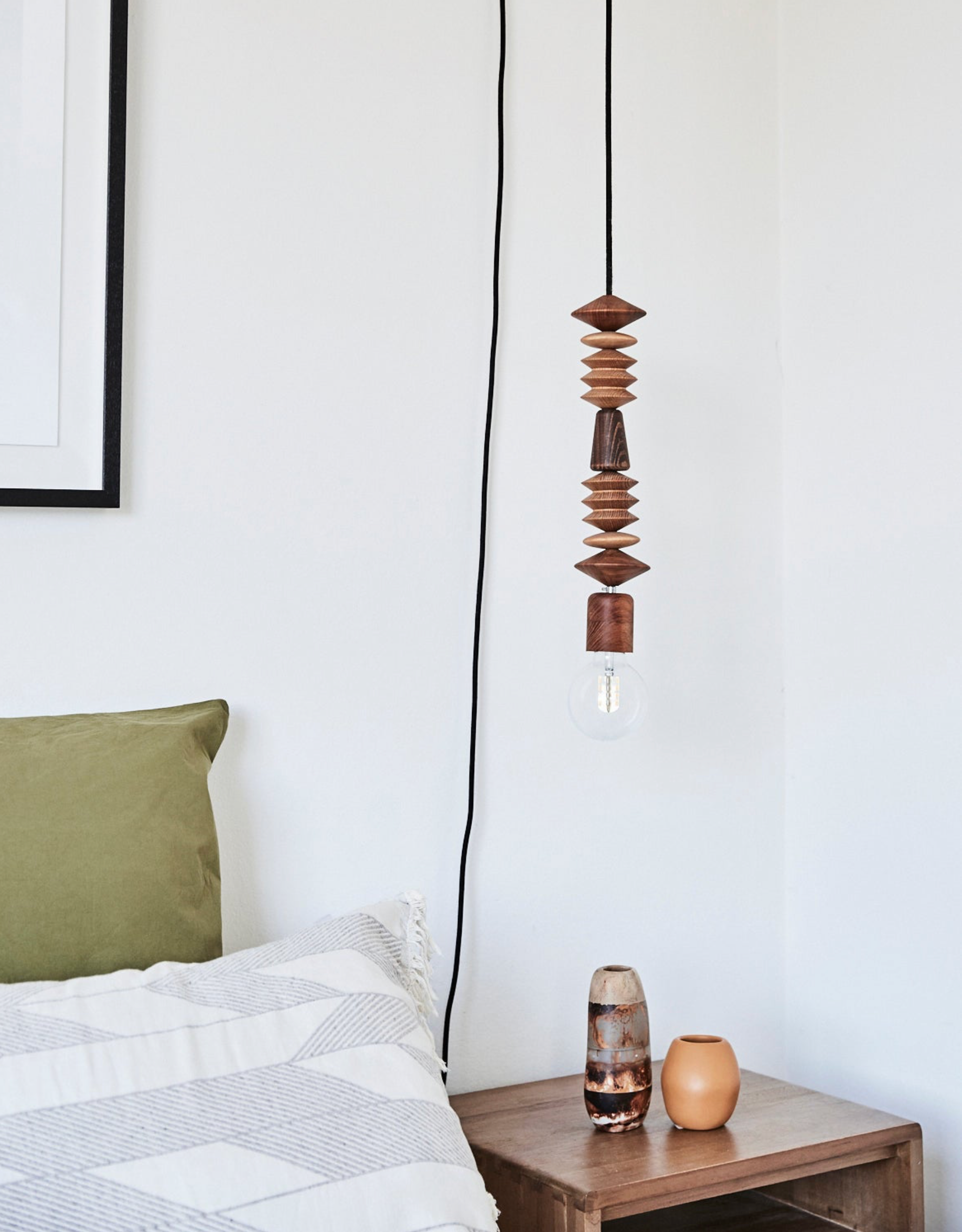 Wooden beaded pendant light hanging above a bed with a minimalistic decor.