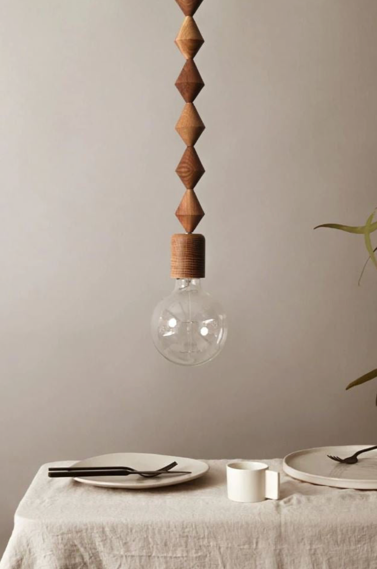 Wooden pendant light hanging above a dining table with plates and cutlery.