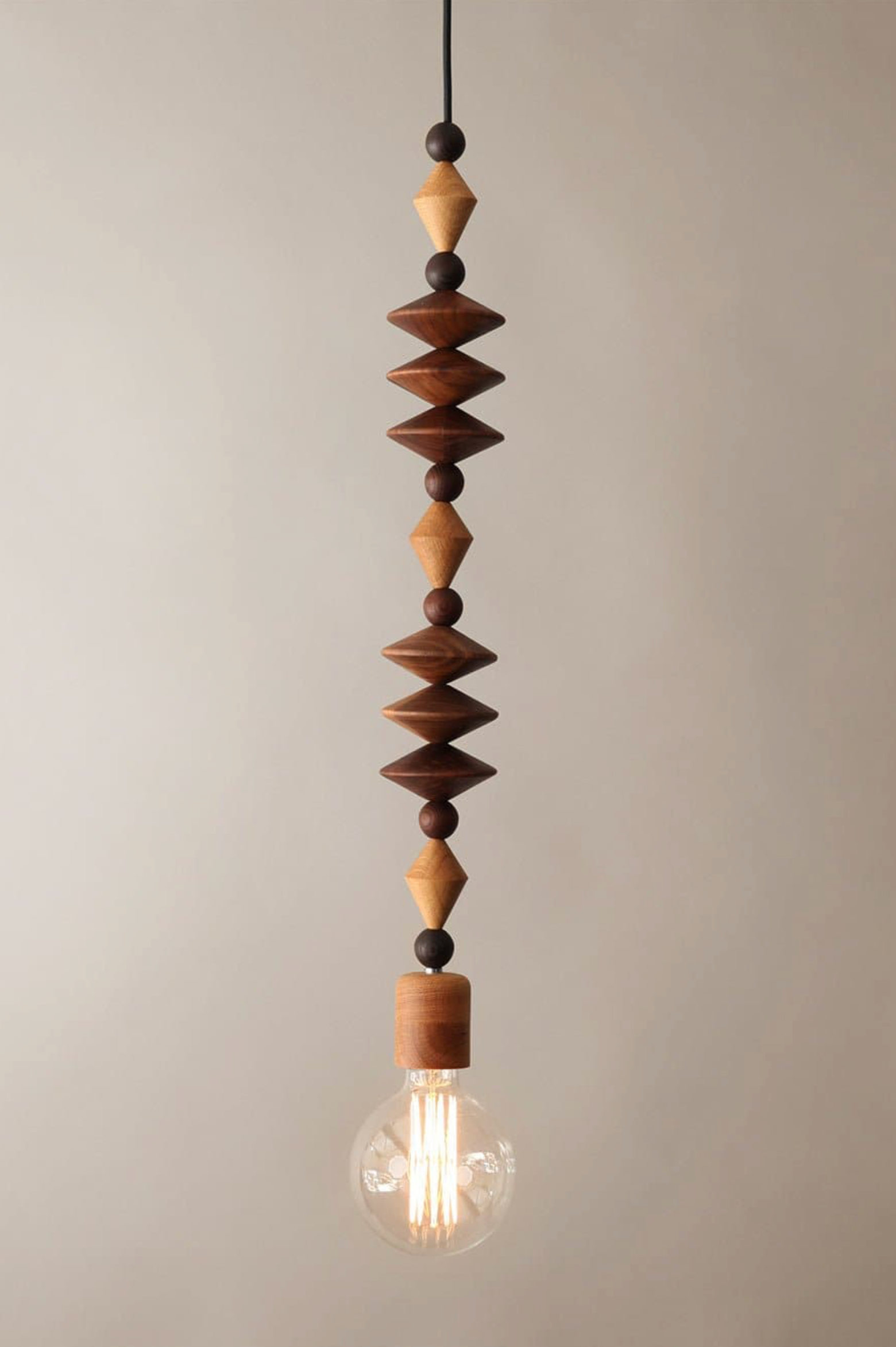 Decorative pendant light with wooden beads and a visible light bulb against a neutral background