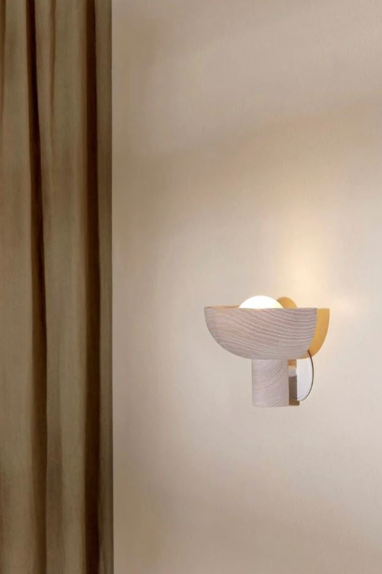 Modern wall sconce on a beige wall with a curtain to the left