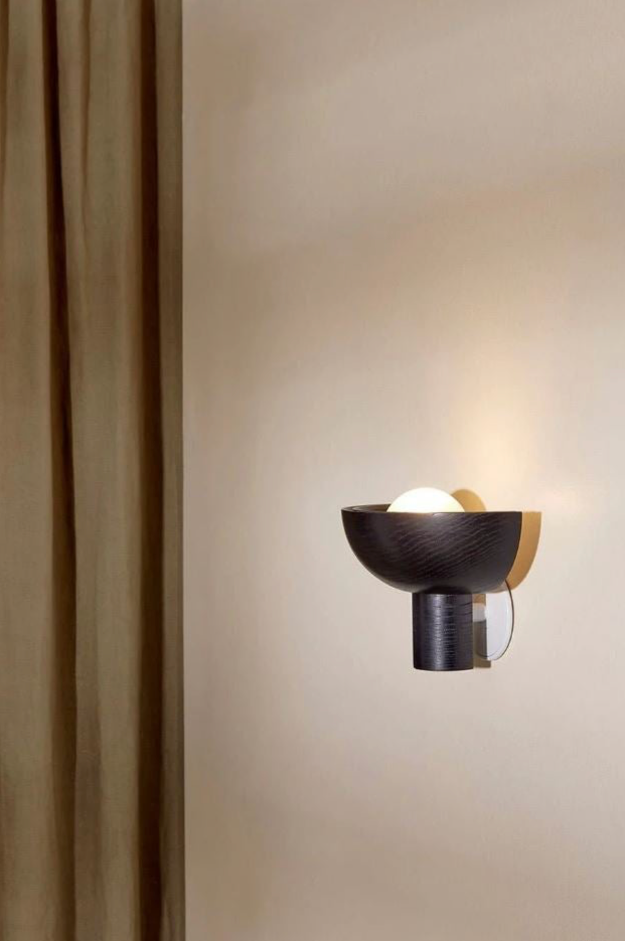 Modern wall sconce on a neutral wall with a curtain to the left.