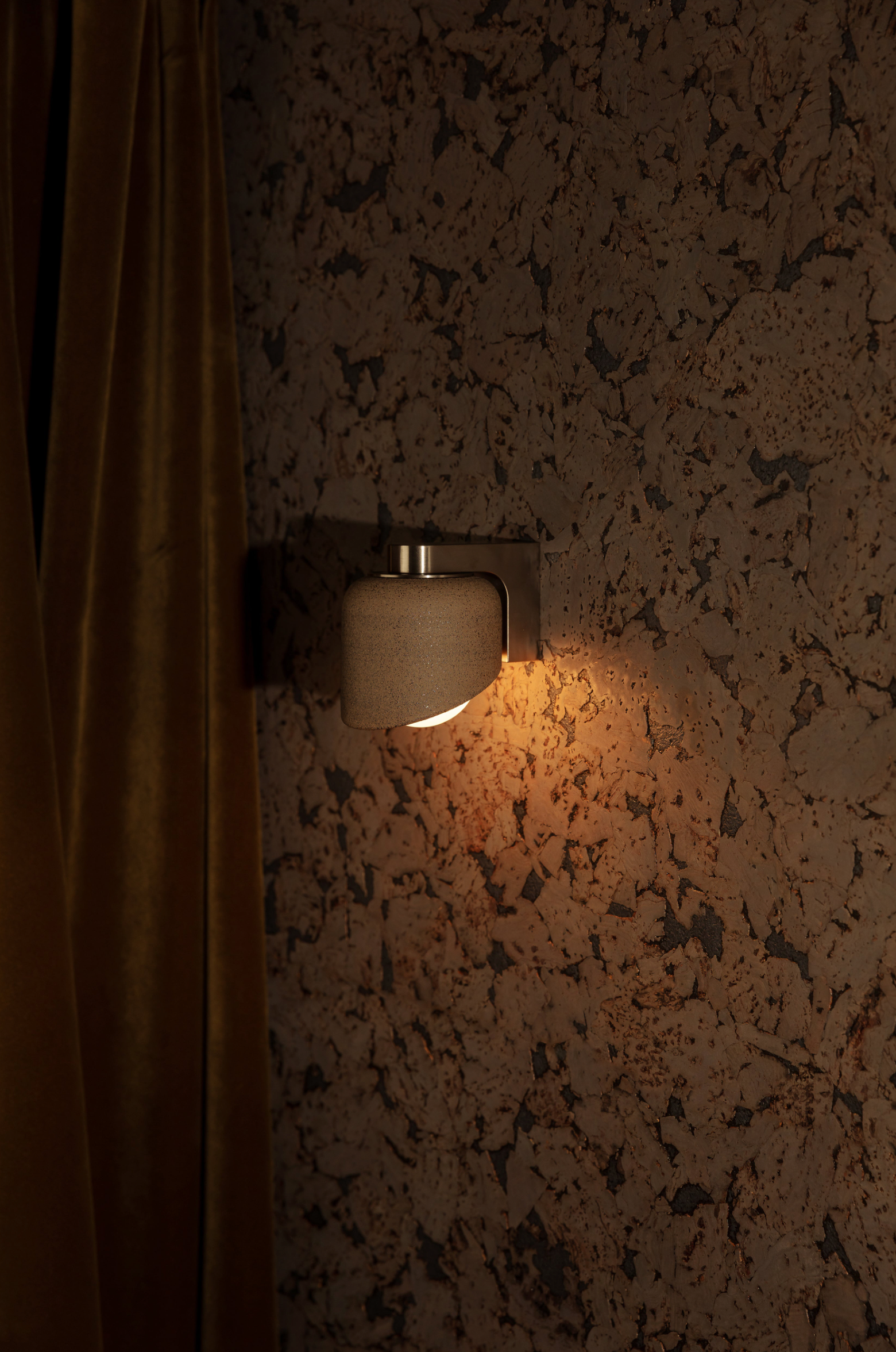 Wall-mounted light fixture on a textured wall with a curtain partially covering it.