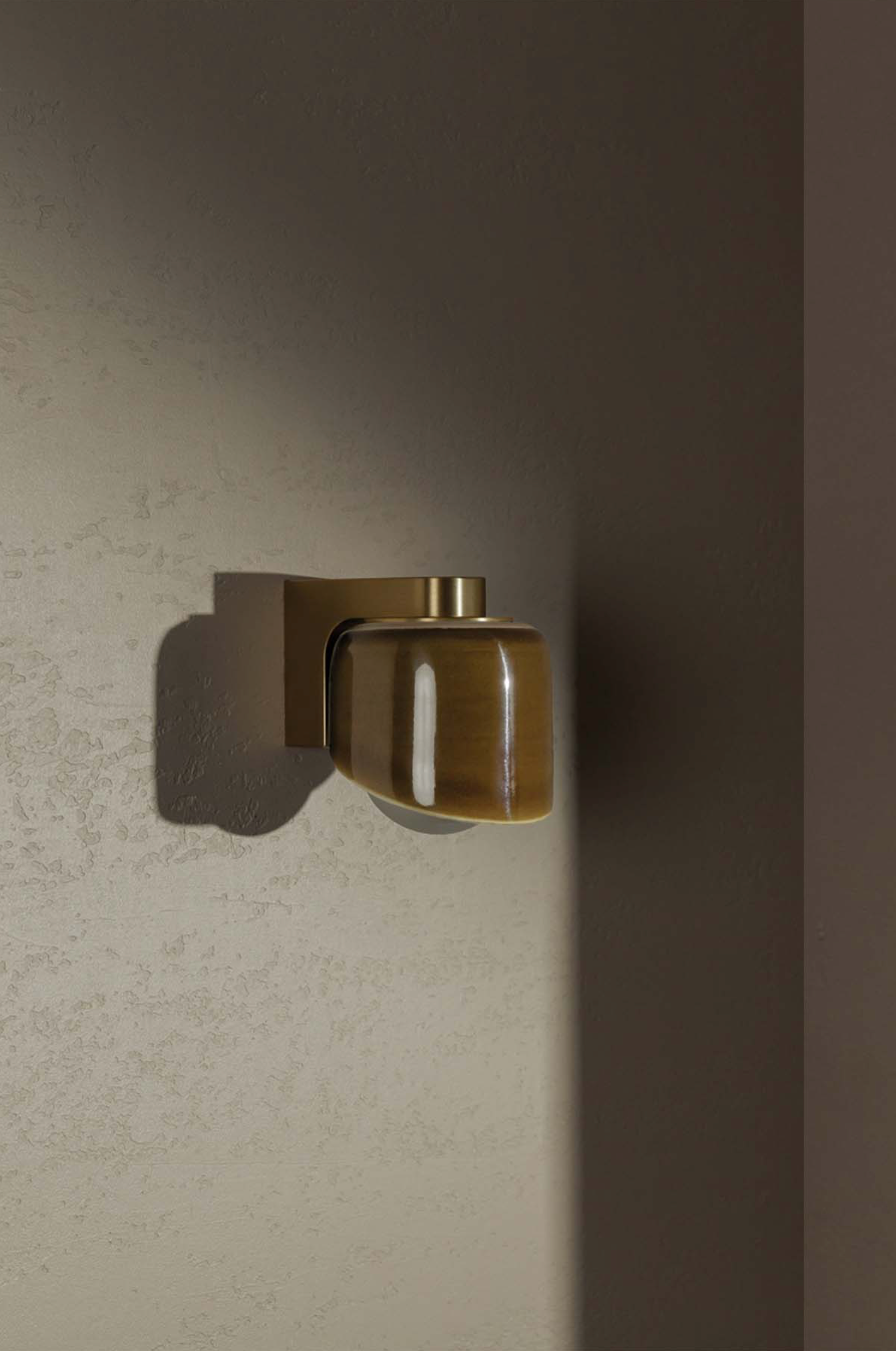 Wall-mounted brass light fixture casting a shadow on a textured wall.