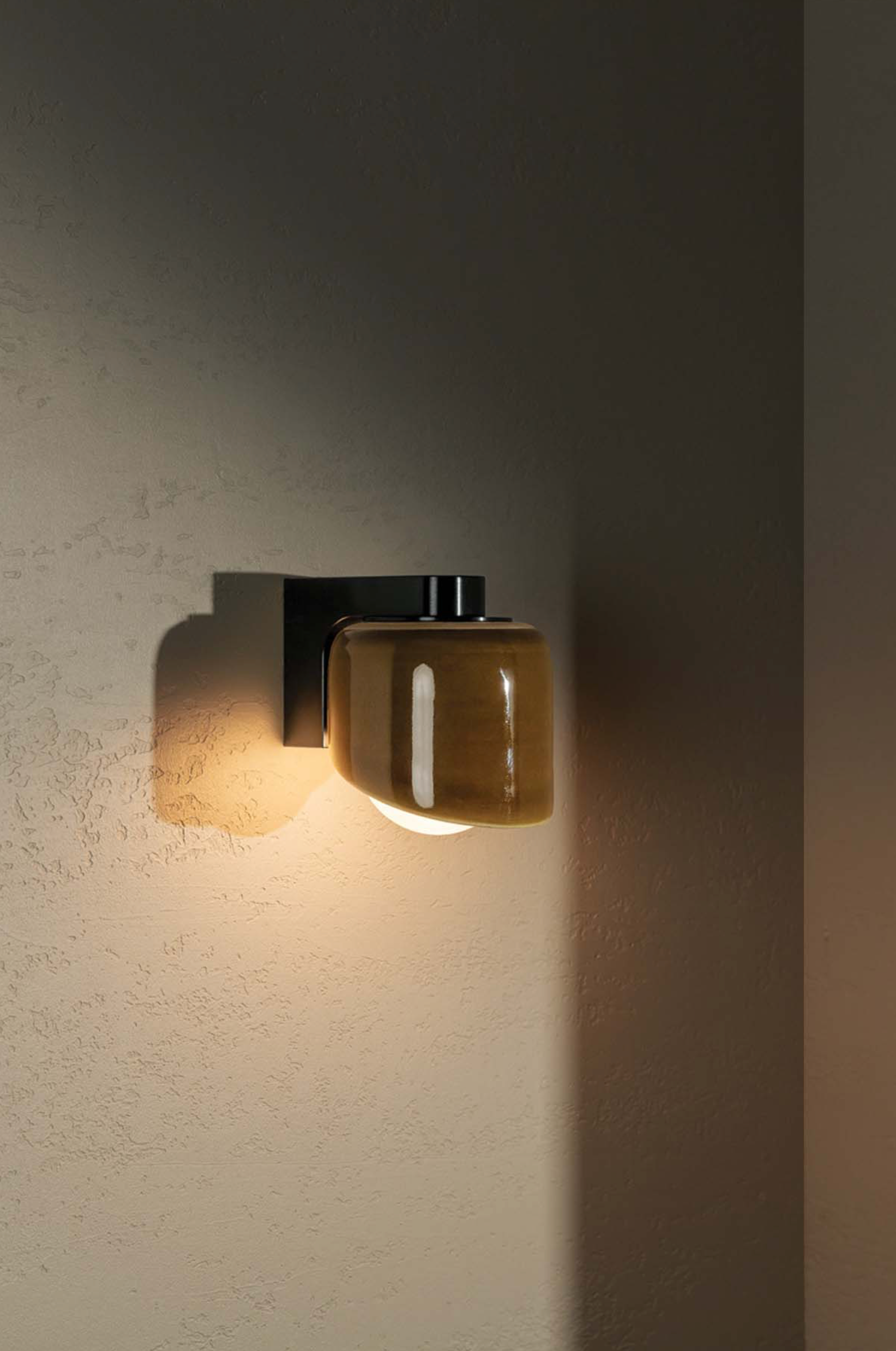 Wall-mounted light fixture with a glass shade on a textured wall.