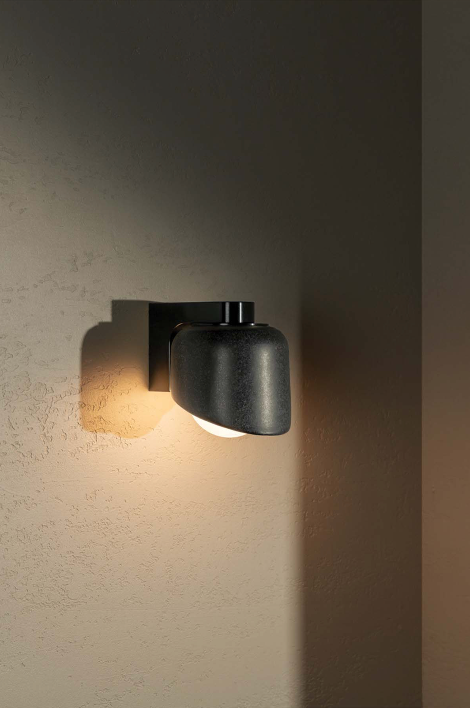 Modern black wall-mounted light fixture on a textured wall.