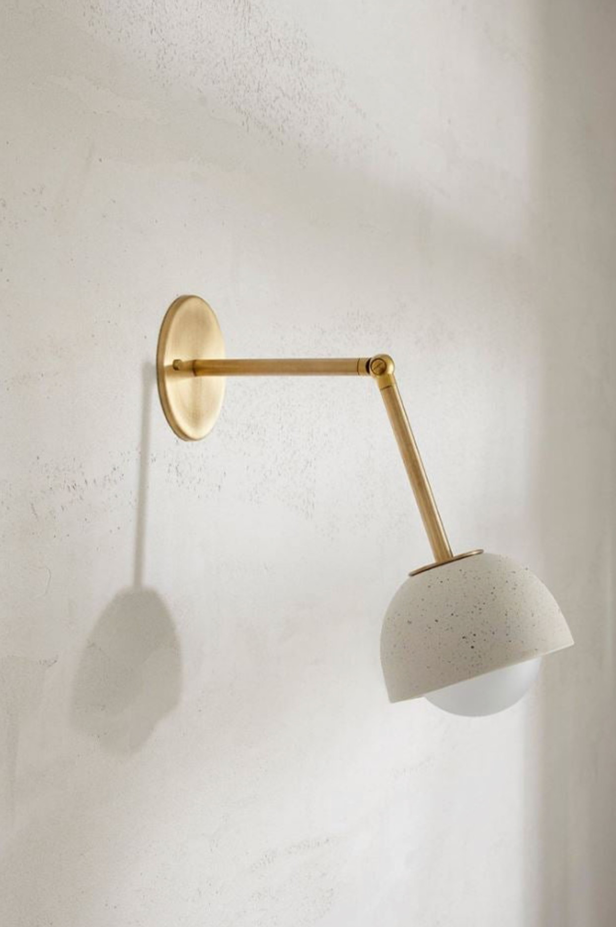 Wall-mounted lamp with brass arm and ceramic shade on a textured wall