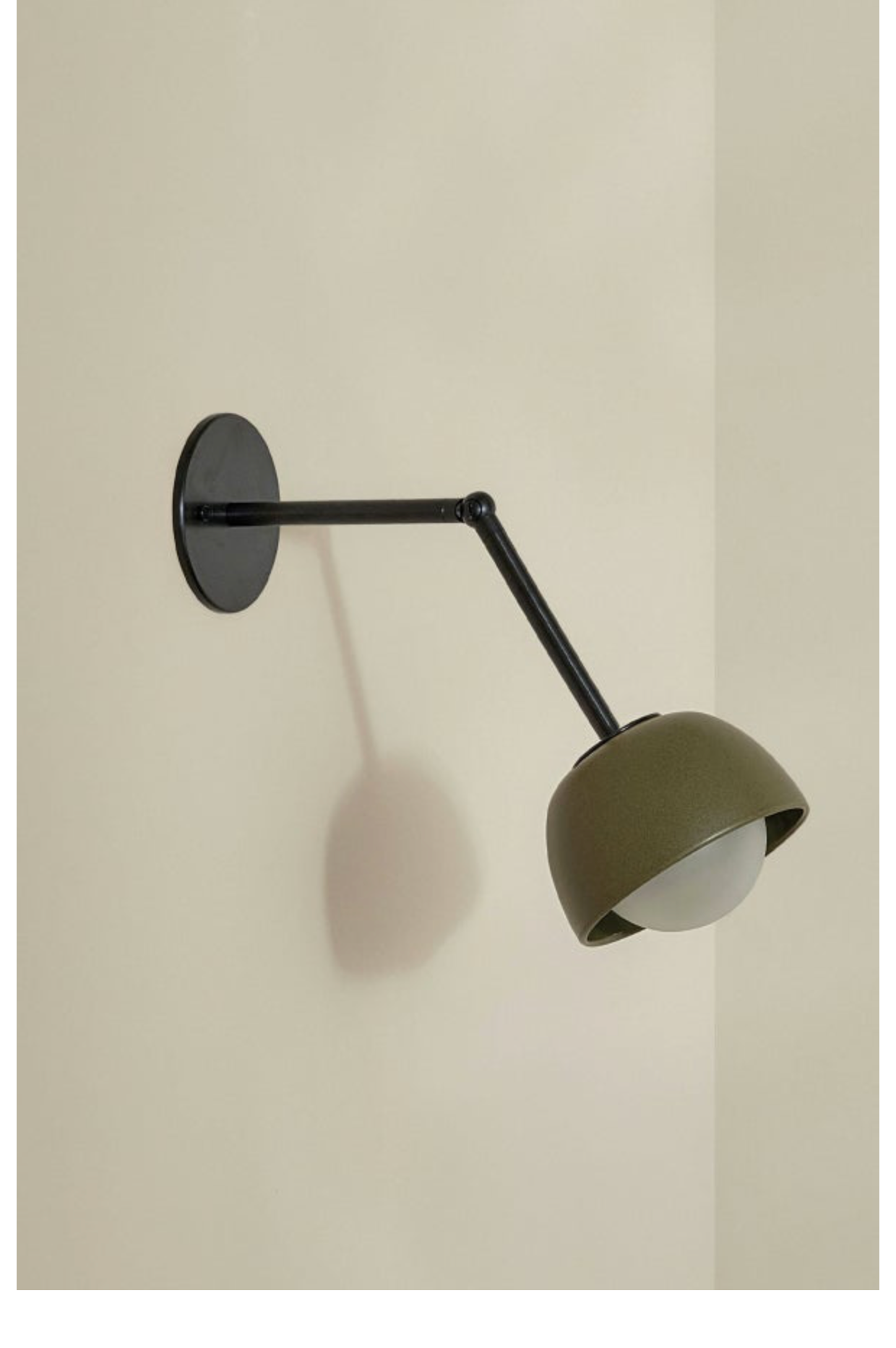 Wall-mounted lamp with a black arm and olive green ceramic shade on a beige wall.