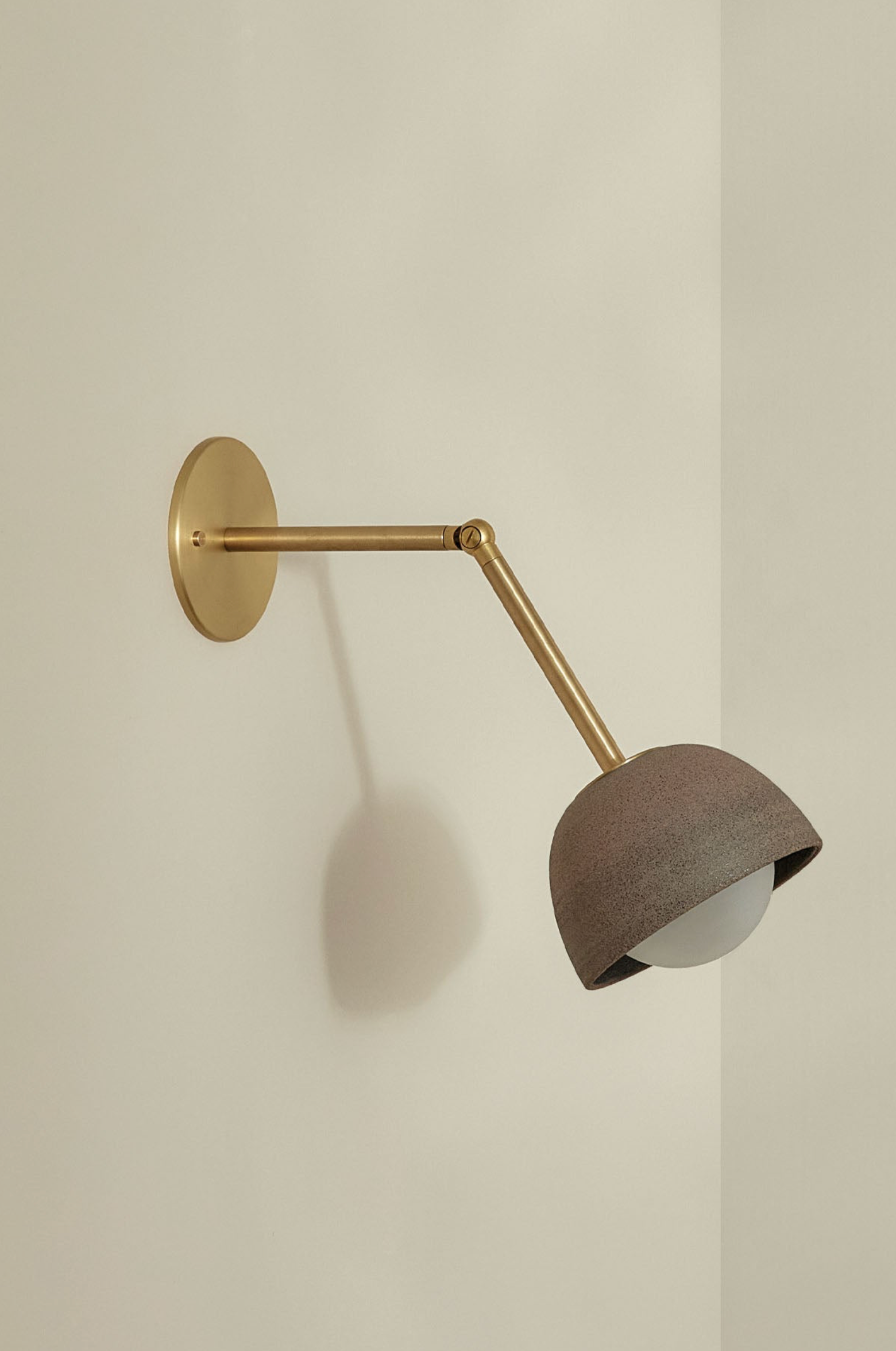Wall-mounted lamp with brass arm and ceramic shade on a plain wall