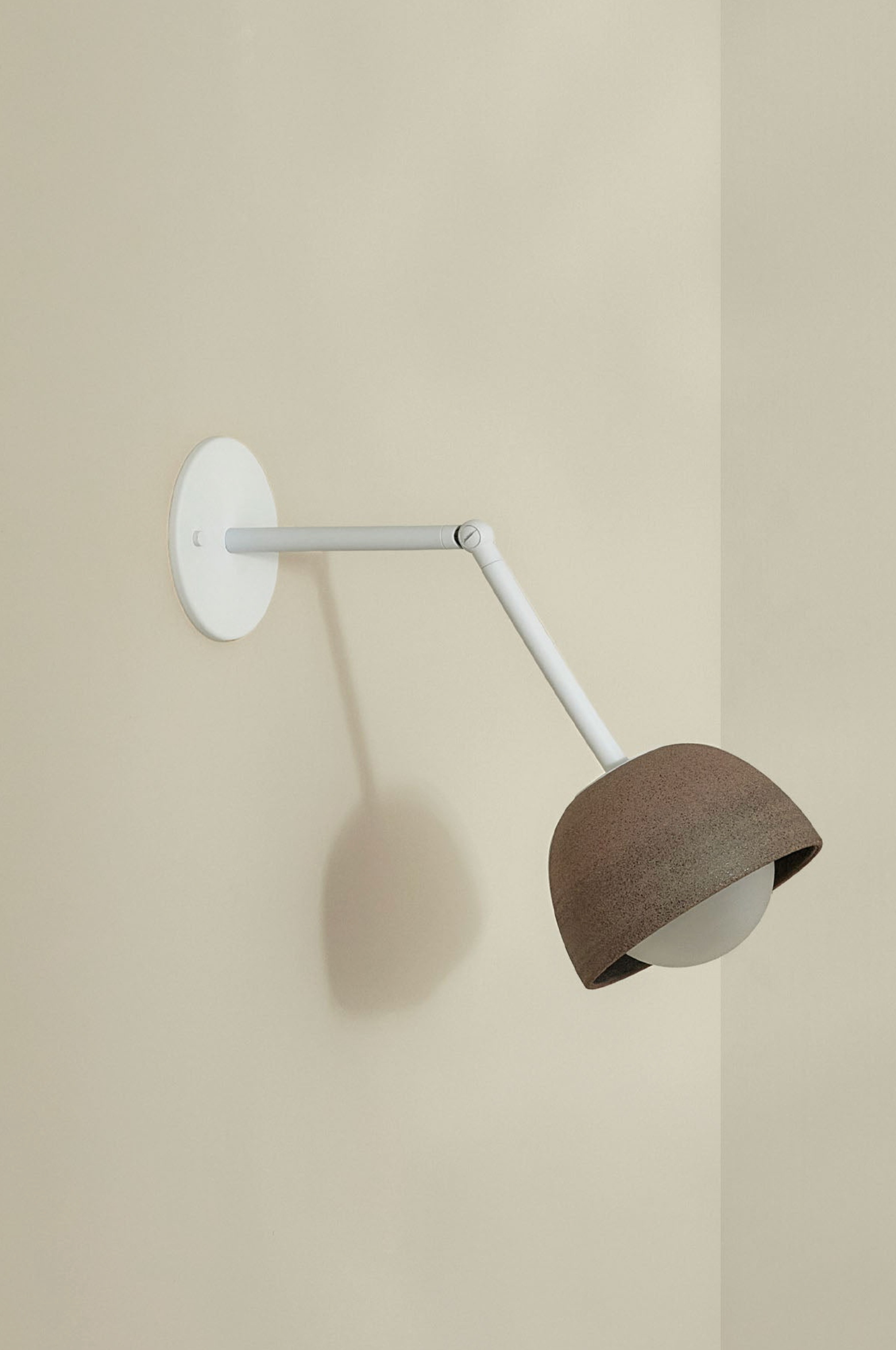 Wall-mounted lamp with a brown shade and white arm on a beige wall