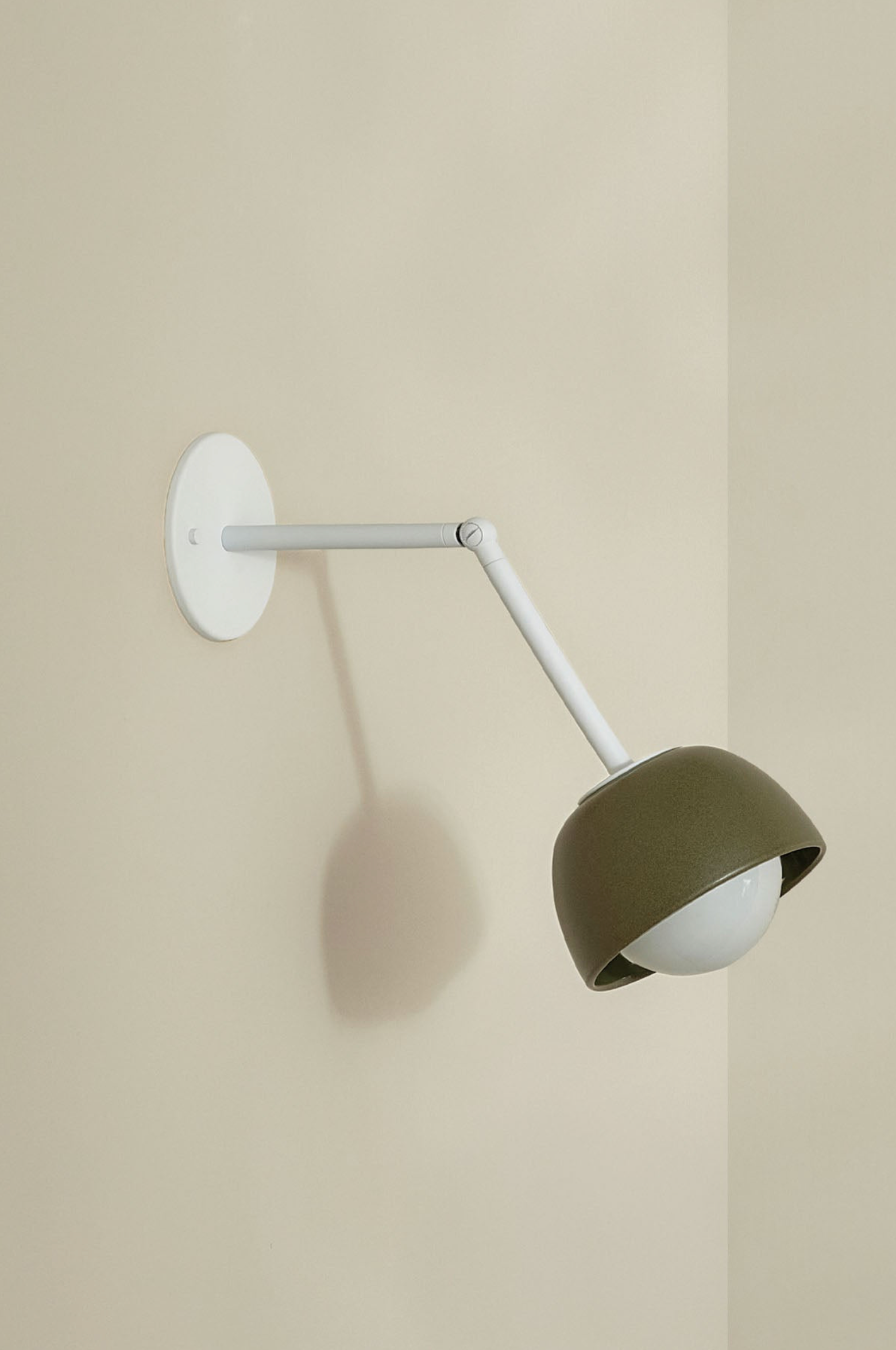 Wall-mounted lamp with a green ceramic shade and white arm on a beige wall