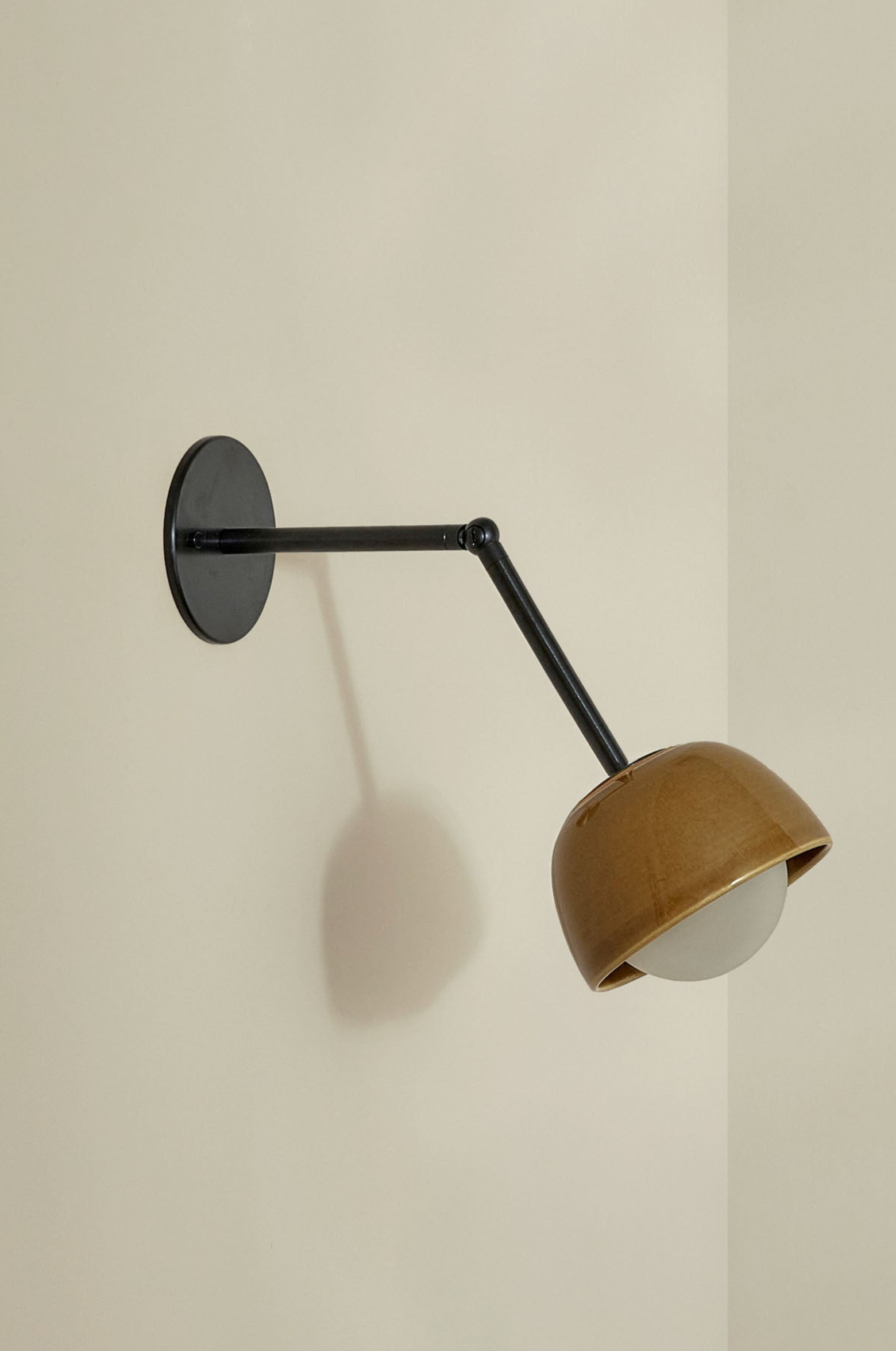 Wall-mounted lamp with brown ceramic glazed shade and black arm on a beige wall