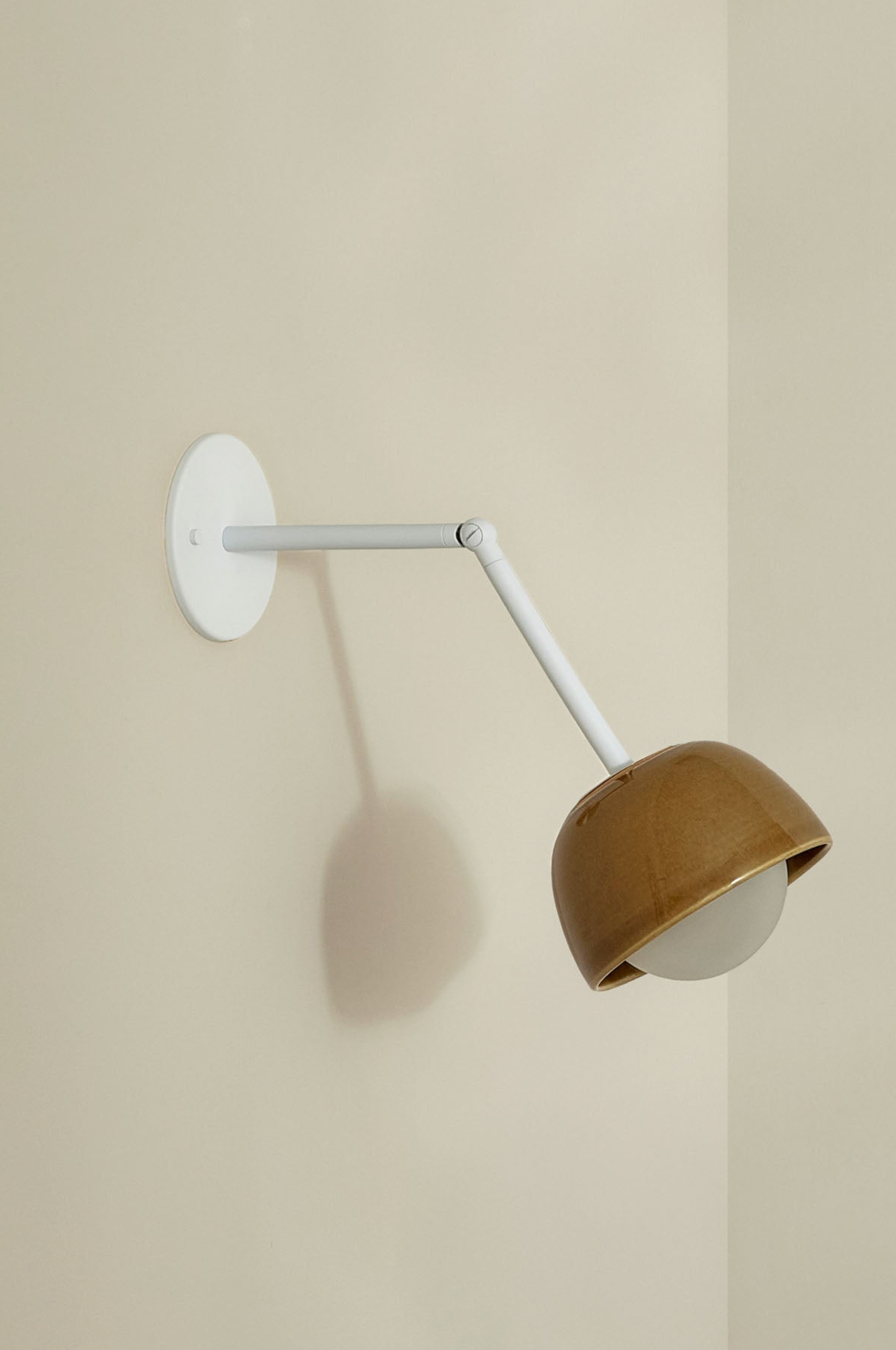 Wall-mounted lamp with brown shade and white arm on a beige wall