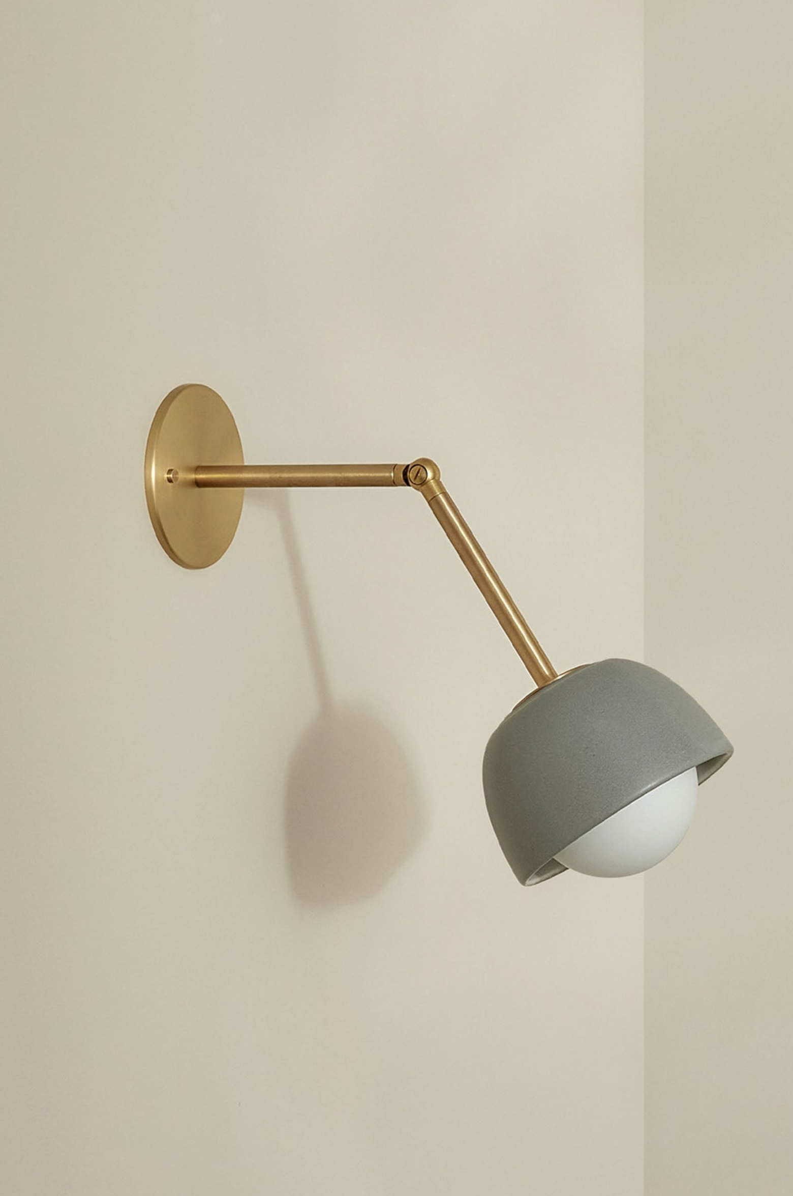 Wall-mounted lamp with a gray shade and gold arm on a beige wall
