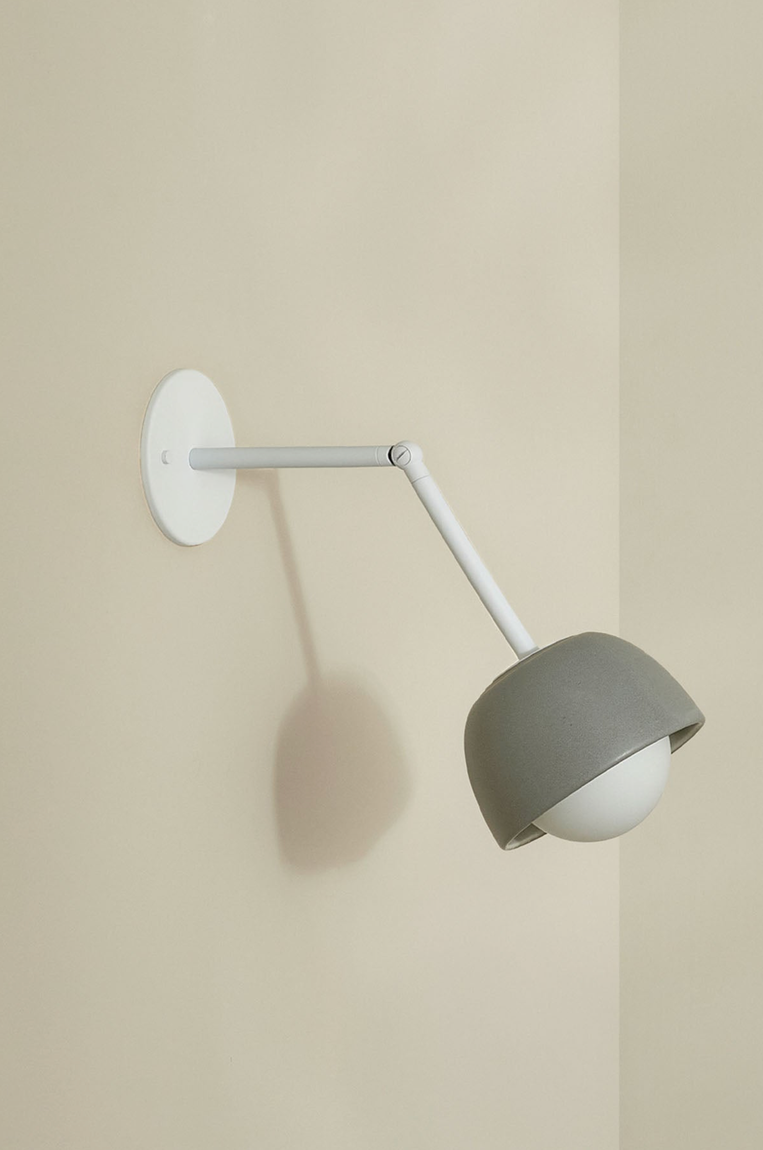 Wall-mounted lamp with a grey ceramic shade and white arm on a beige wall