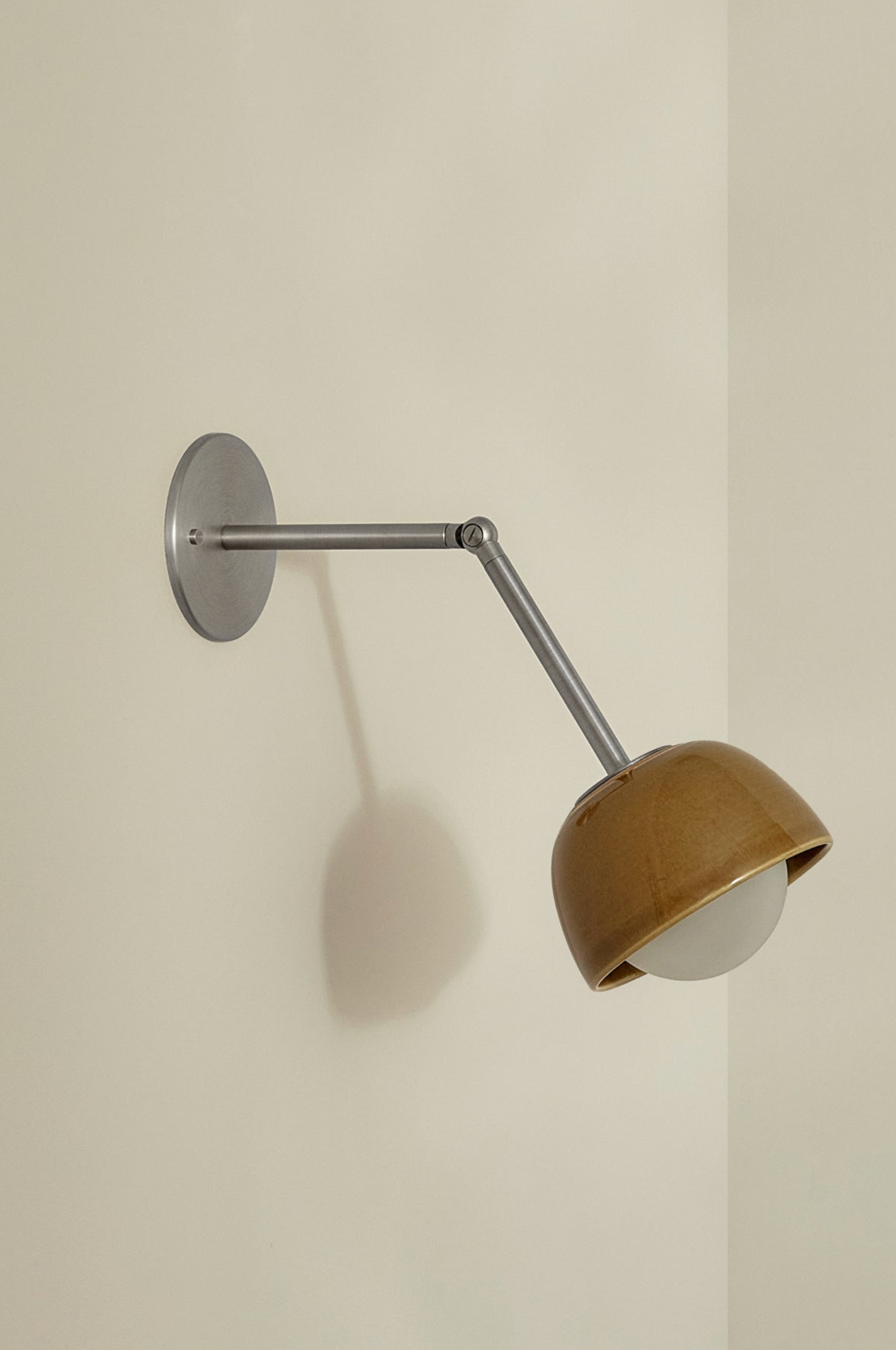Wall-mounted lamp with brown shade and metal arm on a plain wall