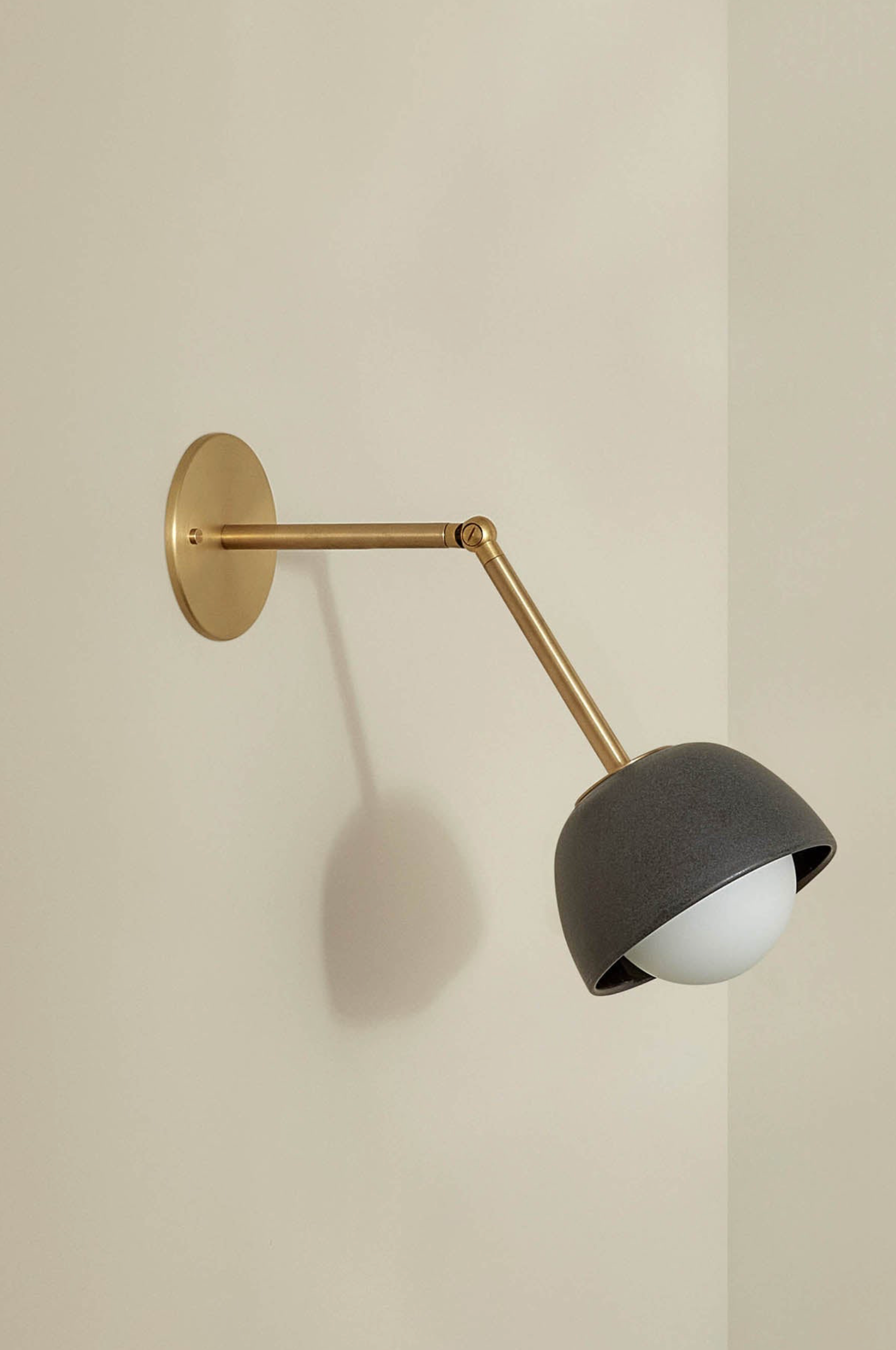 Wall-mounted lamp with black shade and brass arm on a beige wall