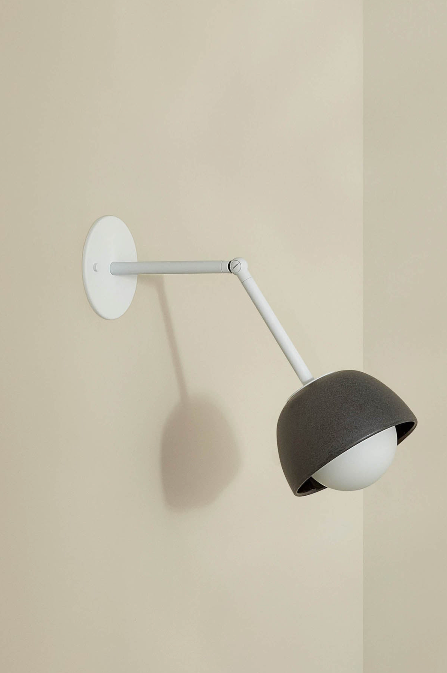 Wall-mounted lamp with a dark shade and white arm on a beige wall