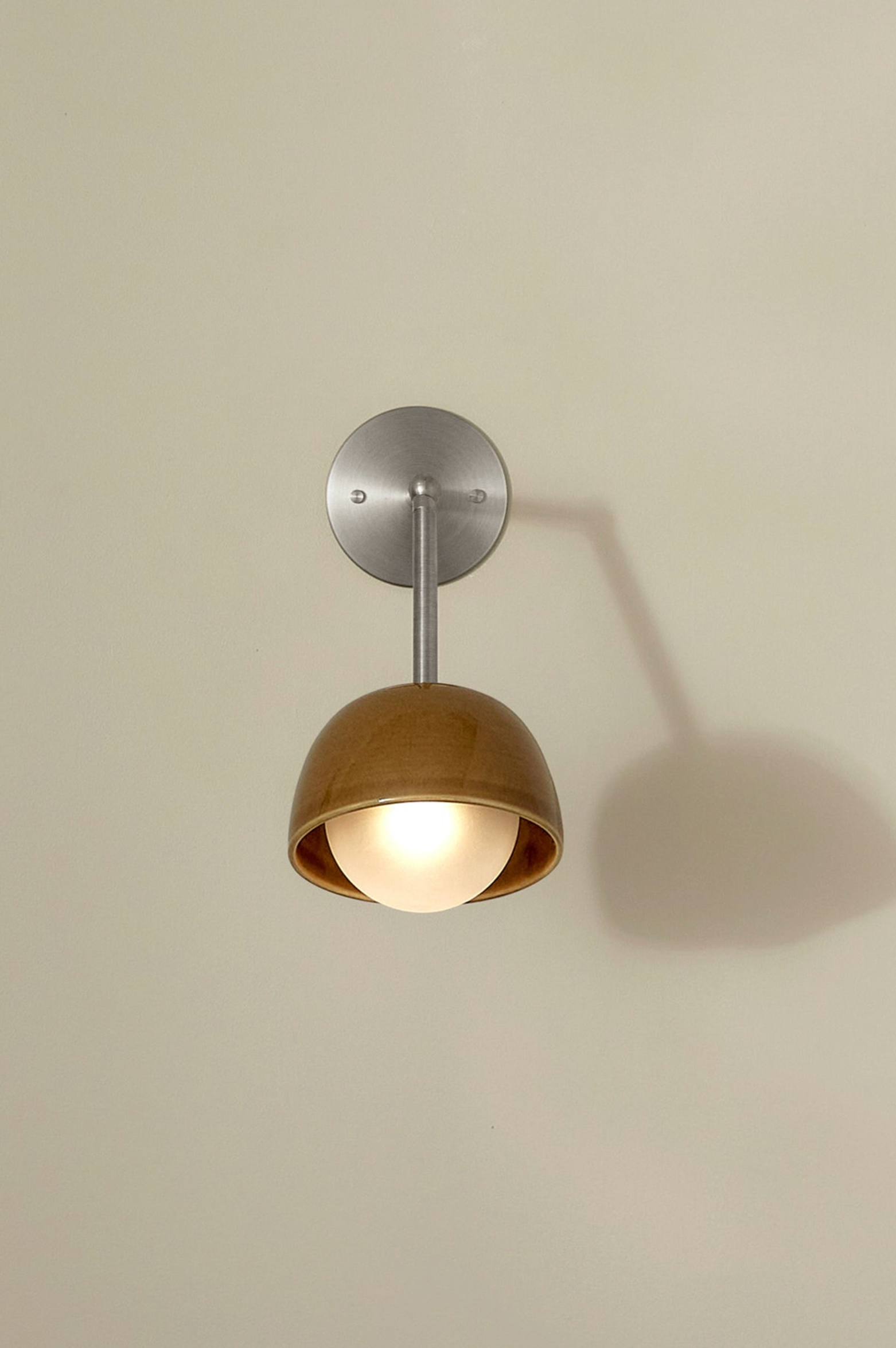 Wall-mounted light fixture with a metallic finish and ceramic shade on a beige wall.