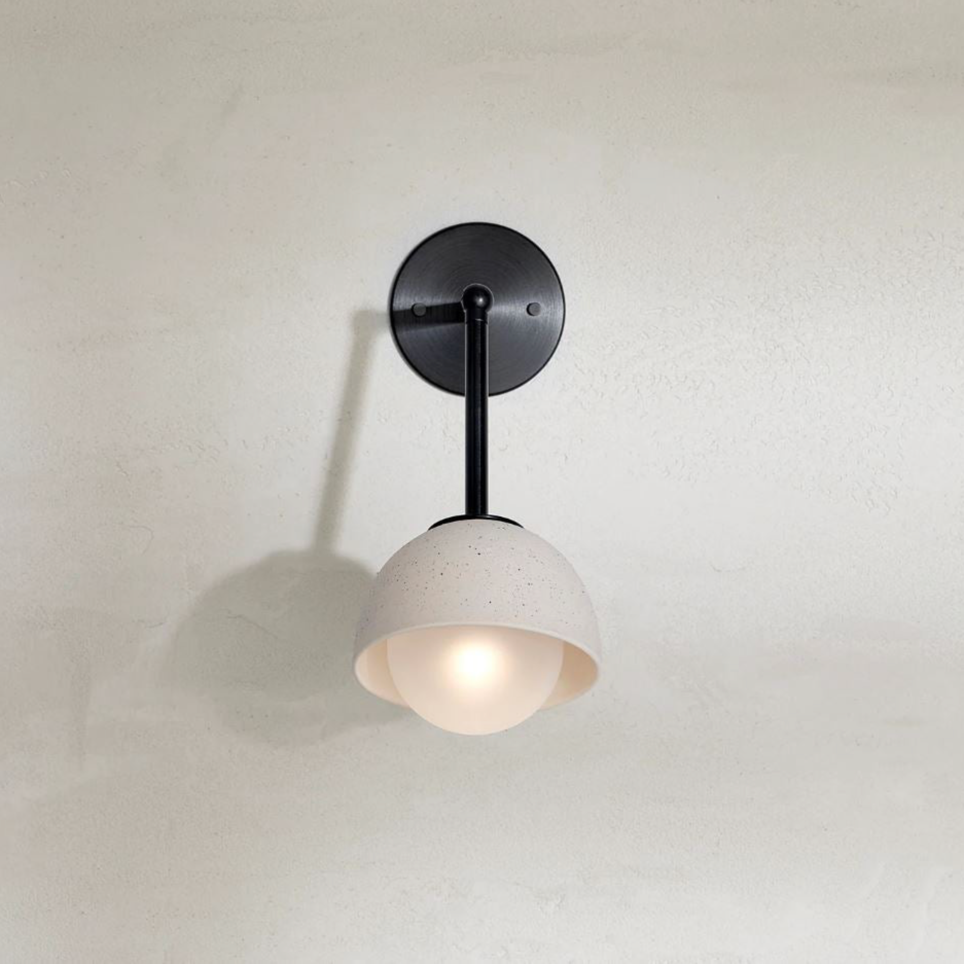 Wall-mounted light fixture with a white shade and black arm on a plain wall.