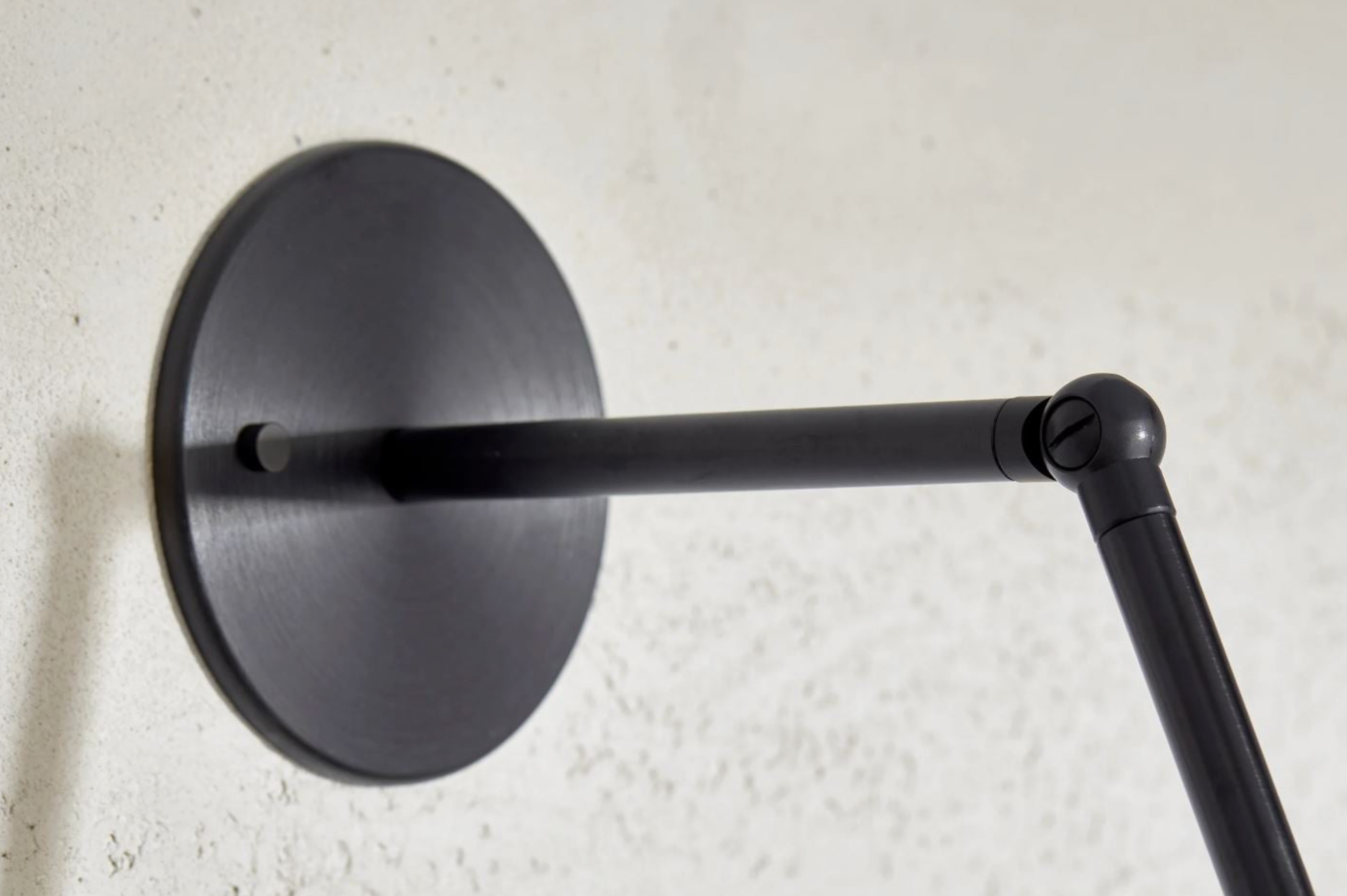 Black wall-mounted lamp with a long arm on a textured white wall