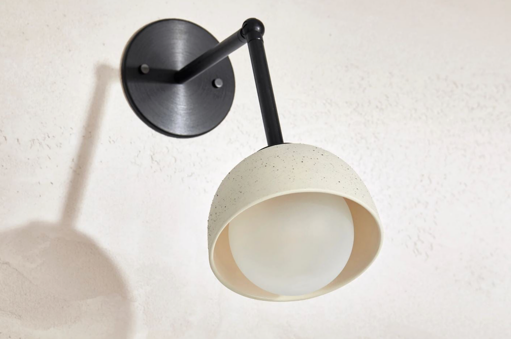 Wall-mounted lamp with a white shade and black arm on a light beige wall.