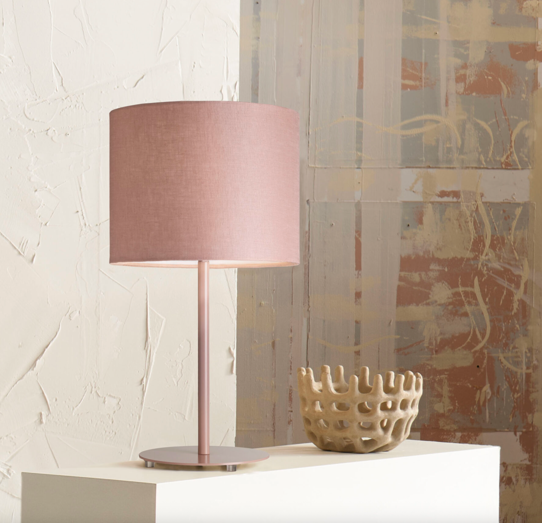 Table lamp with a pink shade on a white surface against a textured wall.