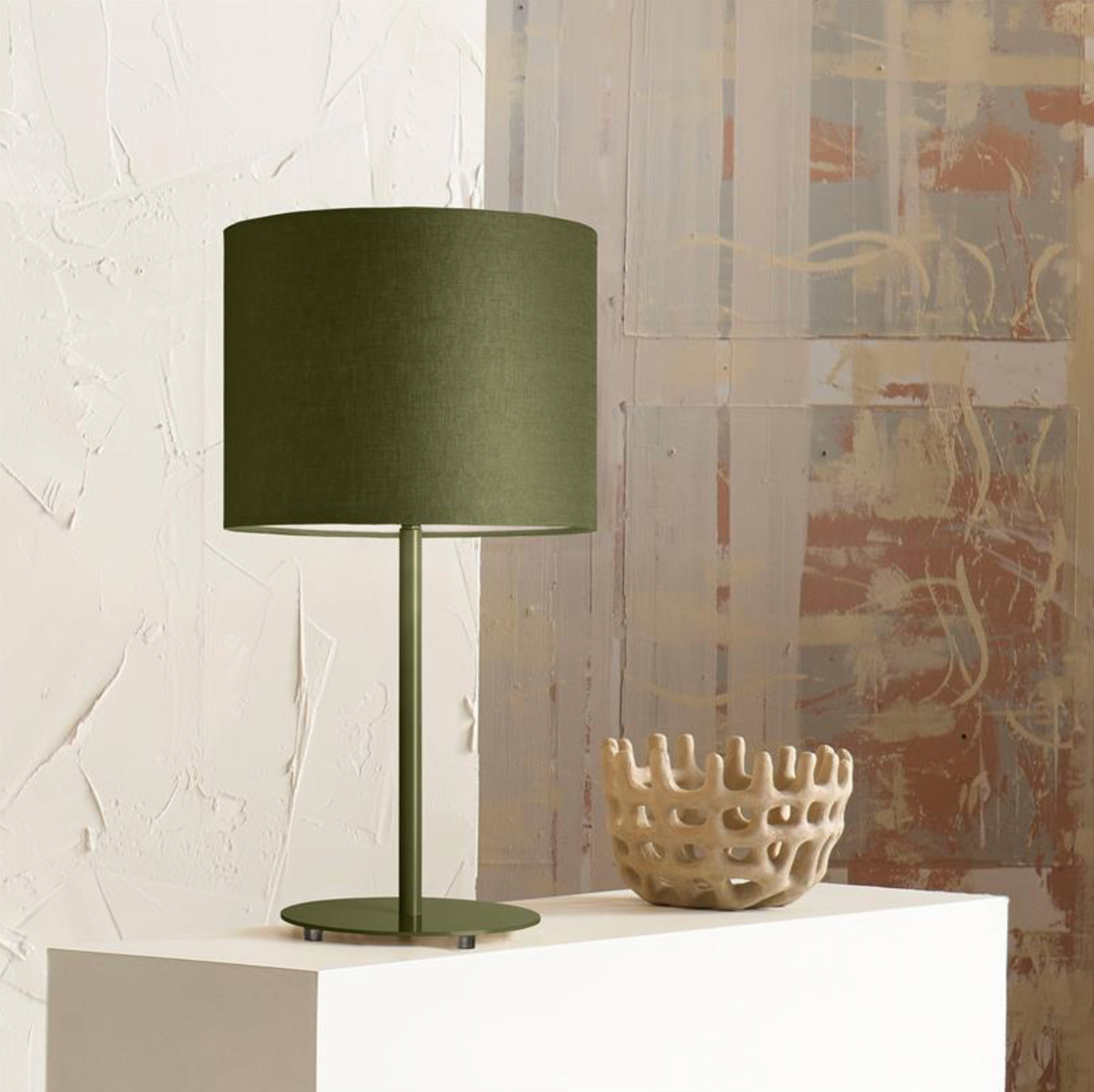 Green table lamp on a white surface with a textured wall and abstract painting in the background