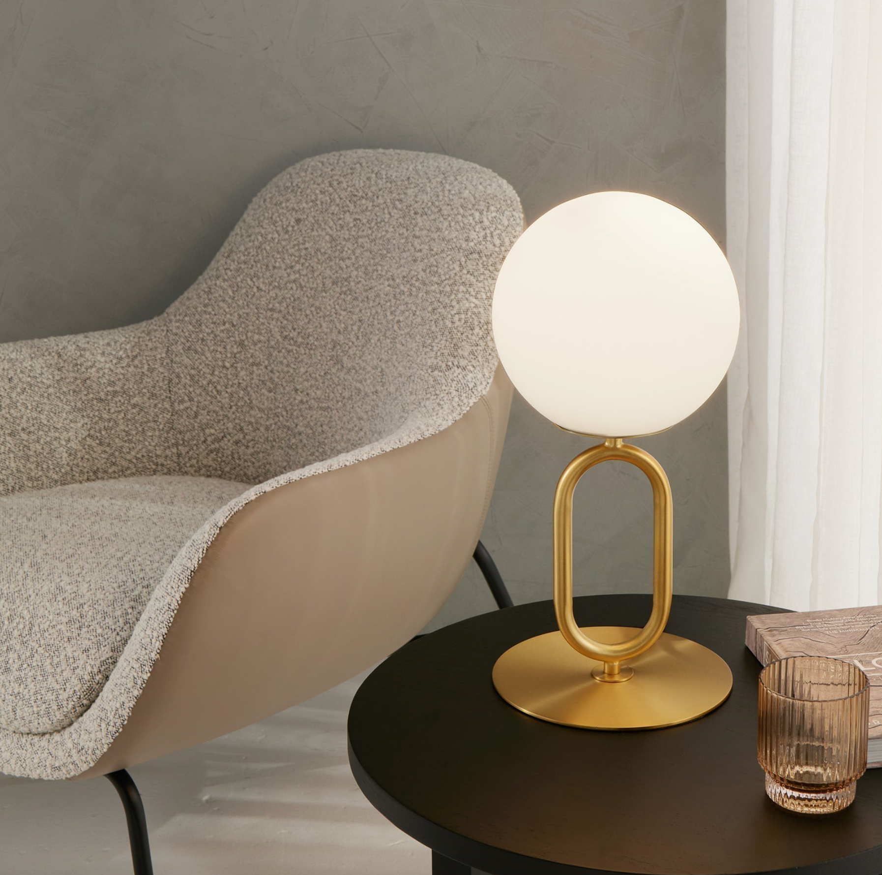 Modern table lamp with gold base on a dark surface next to a textured chair.