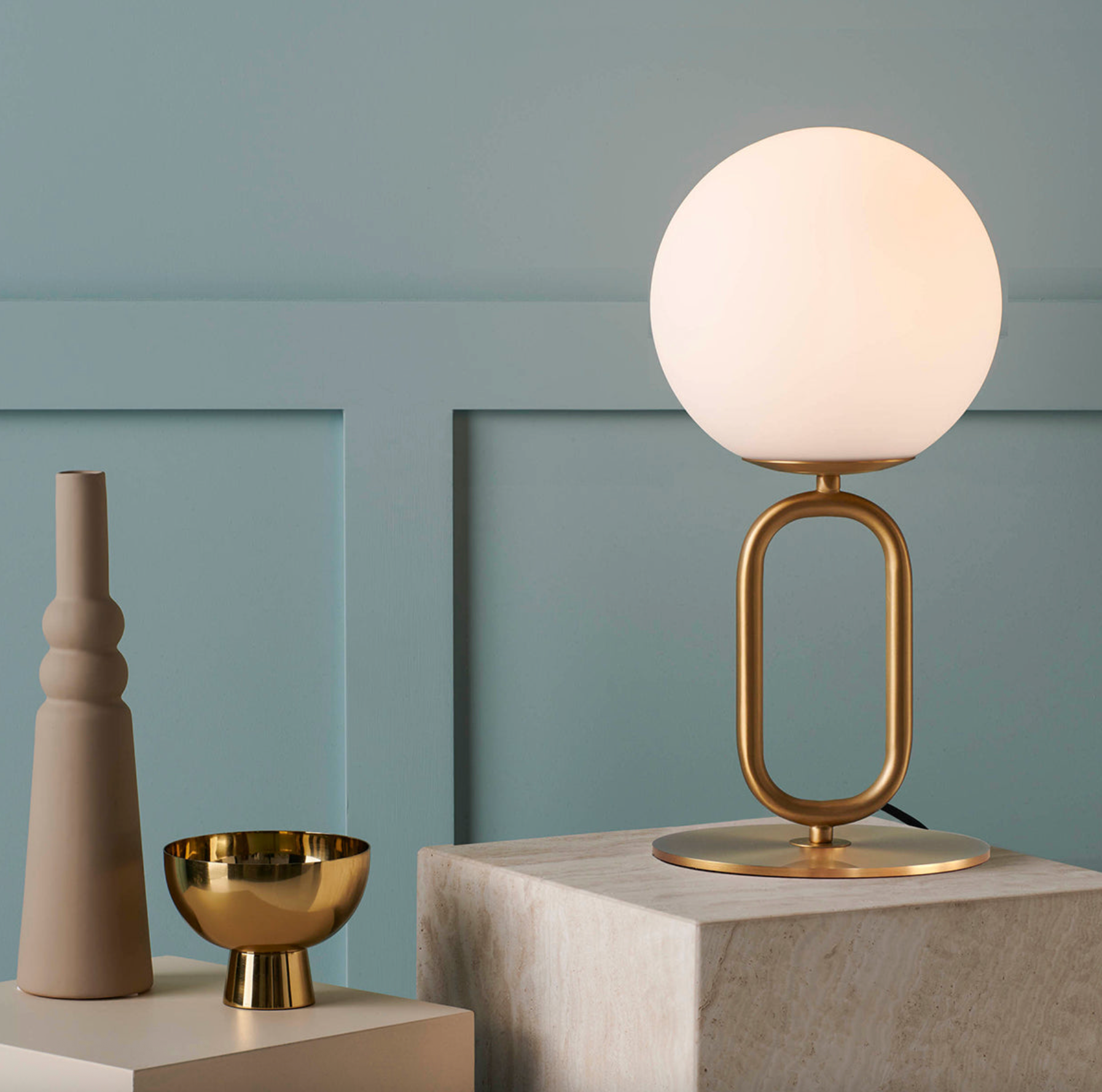 Brass table lamp with a white orb glass shade on a side table with a blue feature wall behind