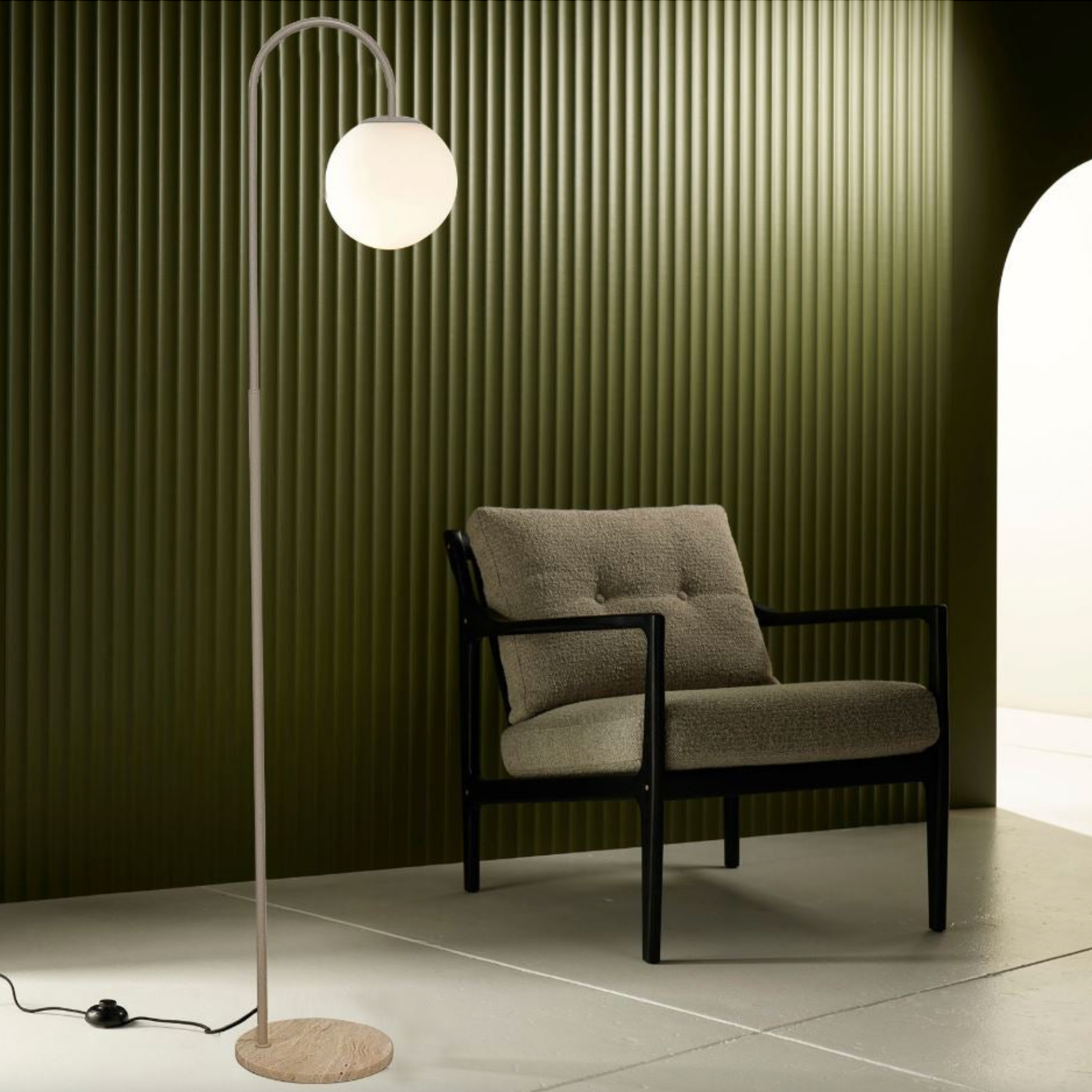 Modern armchair with a floor lamp against a green paneled wall.